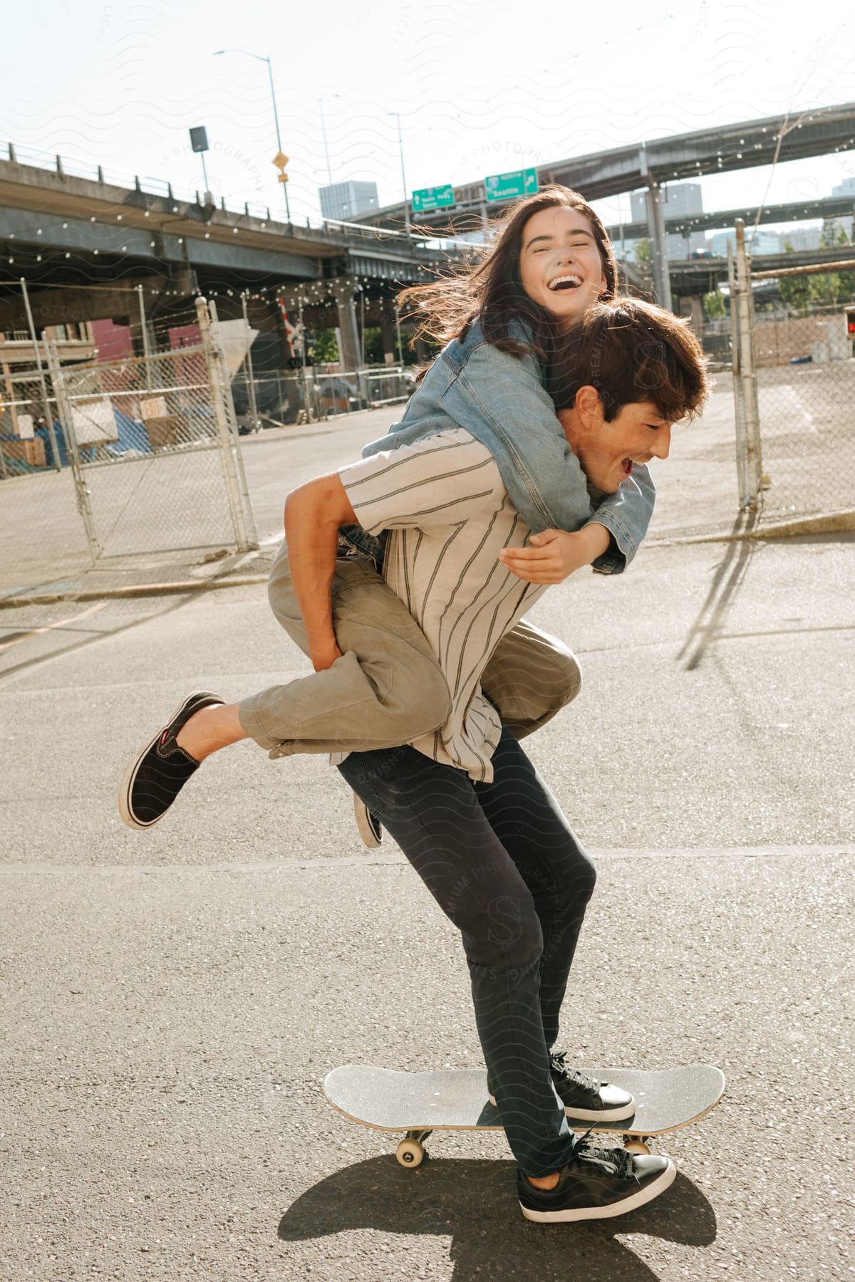 Teenage couple laughing as the boy carries the girl on his back while skateboarding