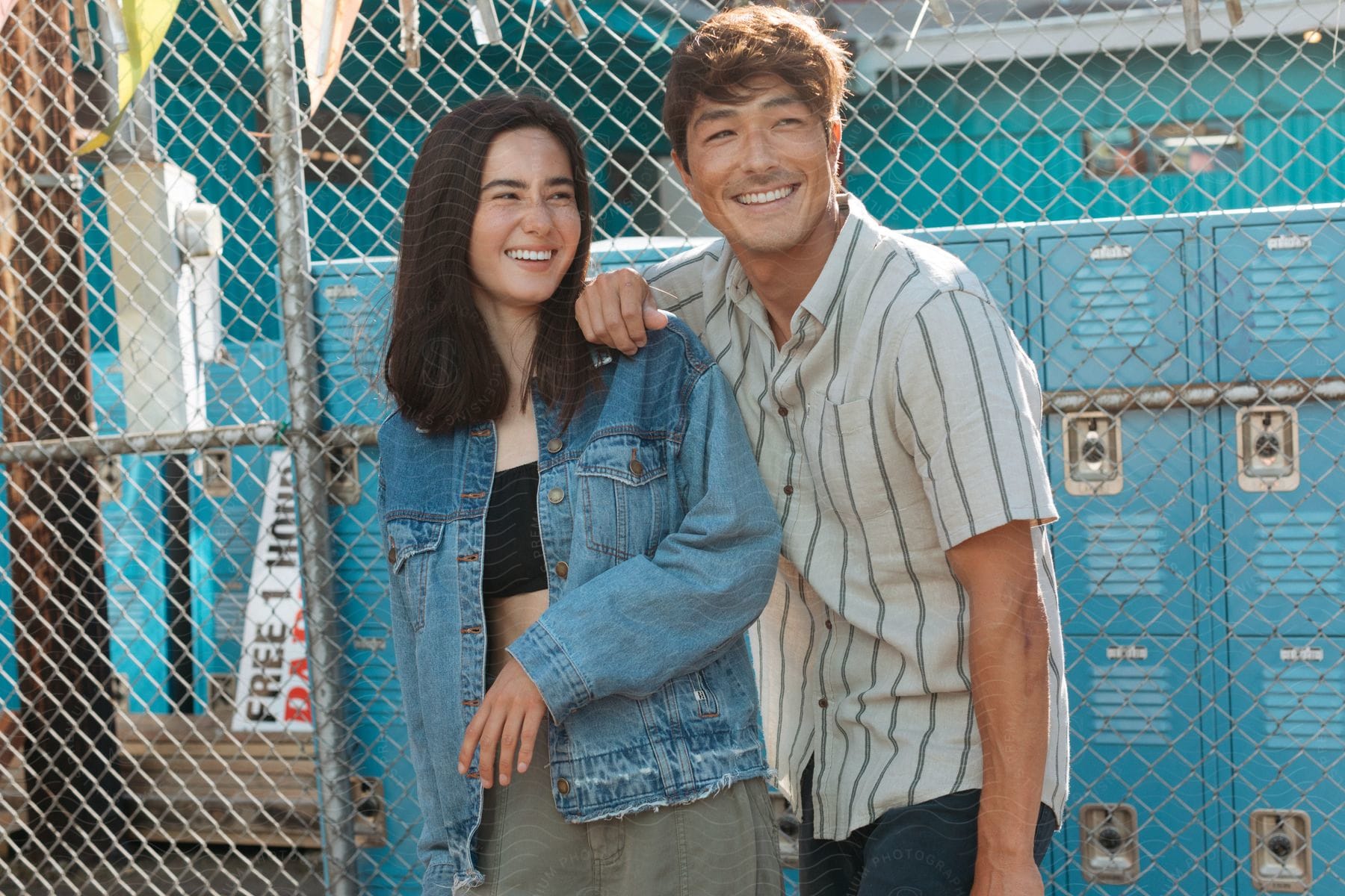 Happy friends standing against chain link fence with blue lockers in the background