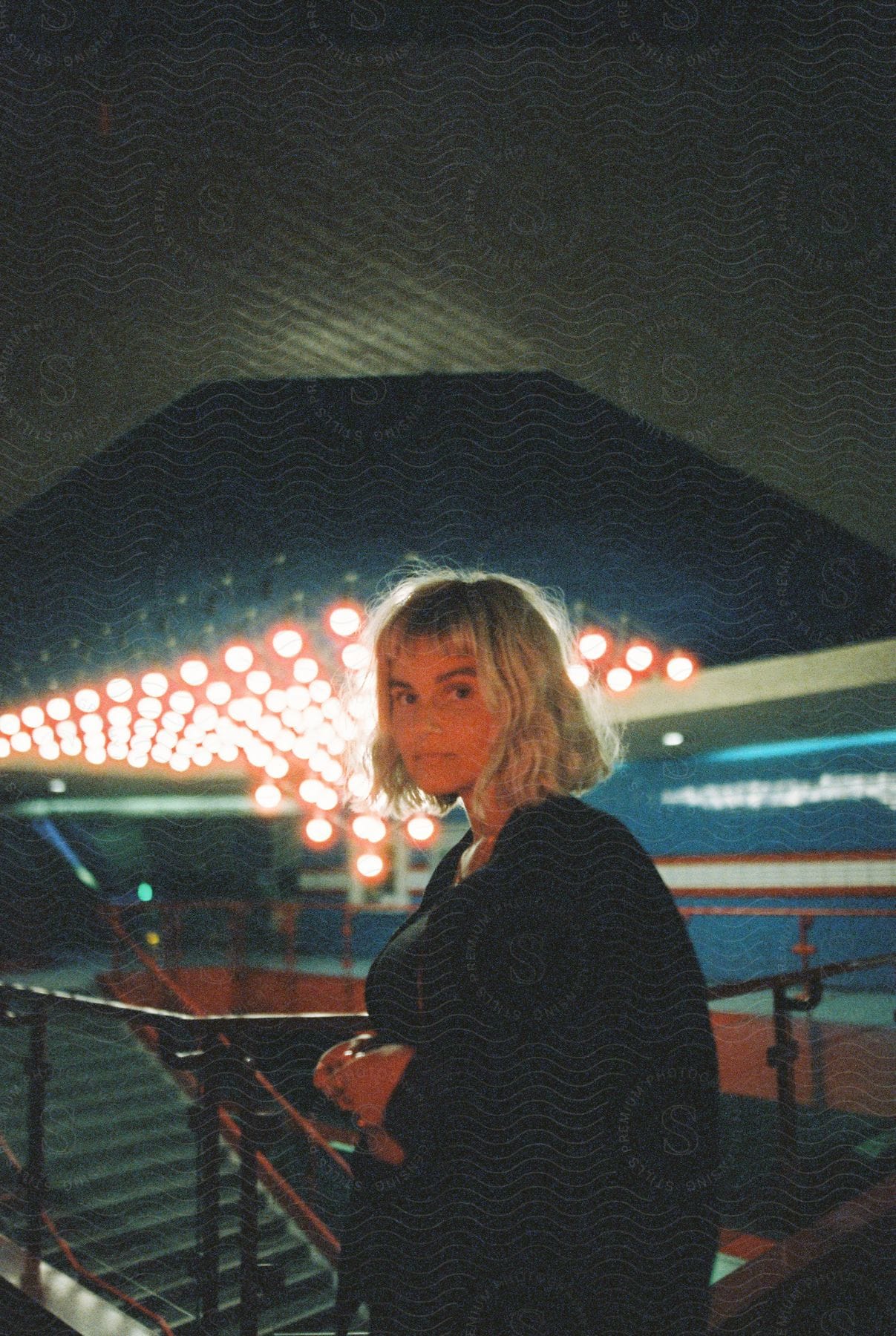 A woman poses near a staircase with no expression on her face