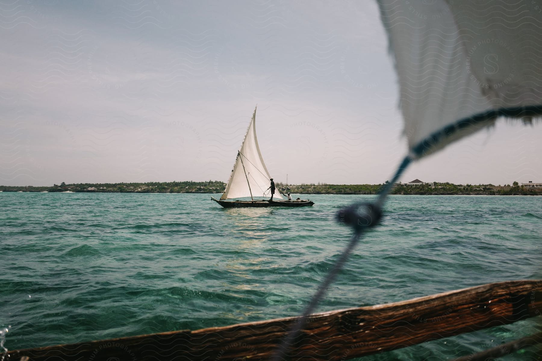 A sailboat is guided by a person over a bay with active waves on a hazy day