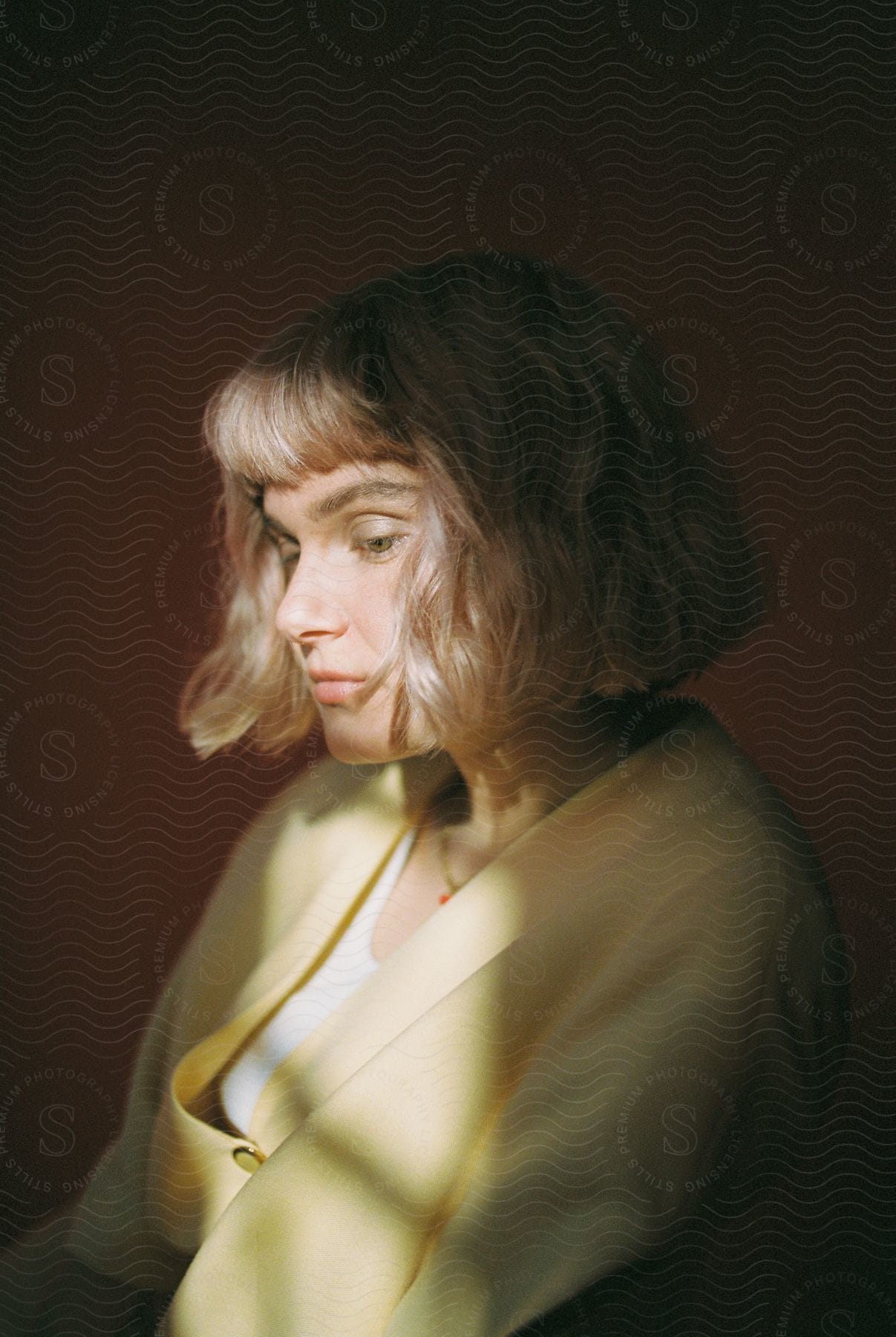 A Woman In A Yellow Coat Looks Down Illuminated By Sunlight From A Window