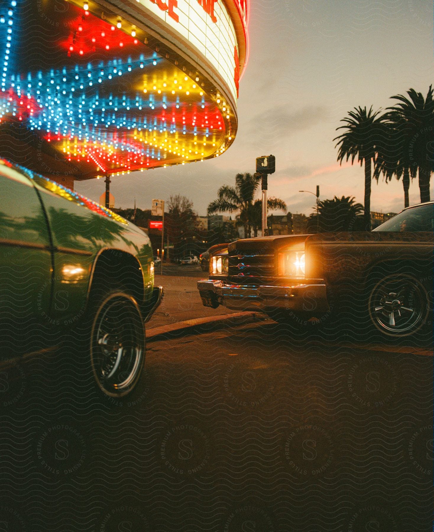 Colorful Movie Theater Sign Above Parked Cars With Palm Trees And Buildings In The Background At Dusk