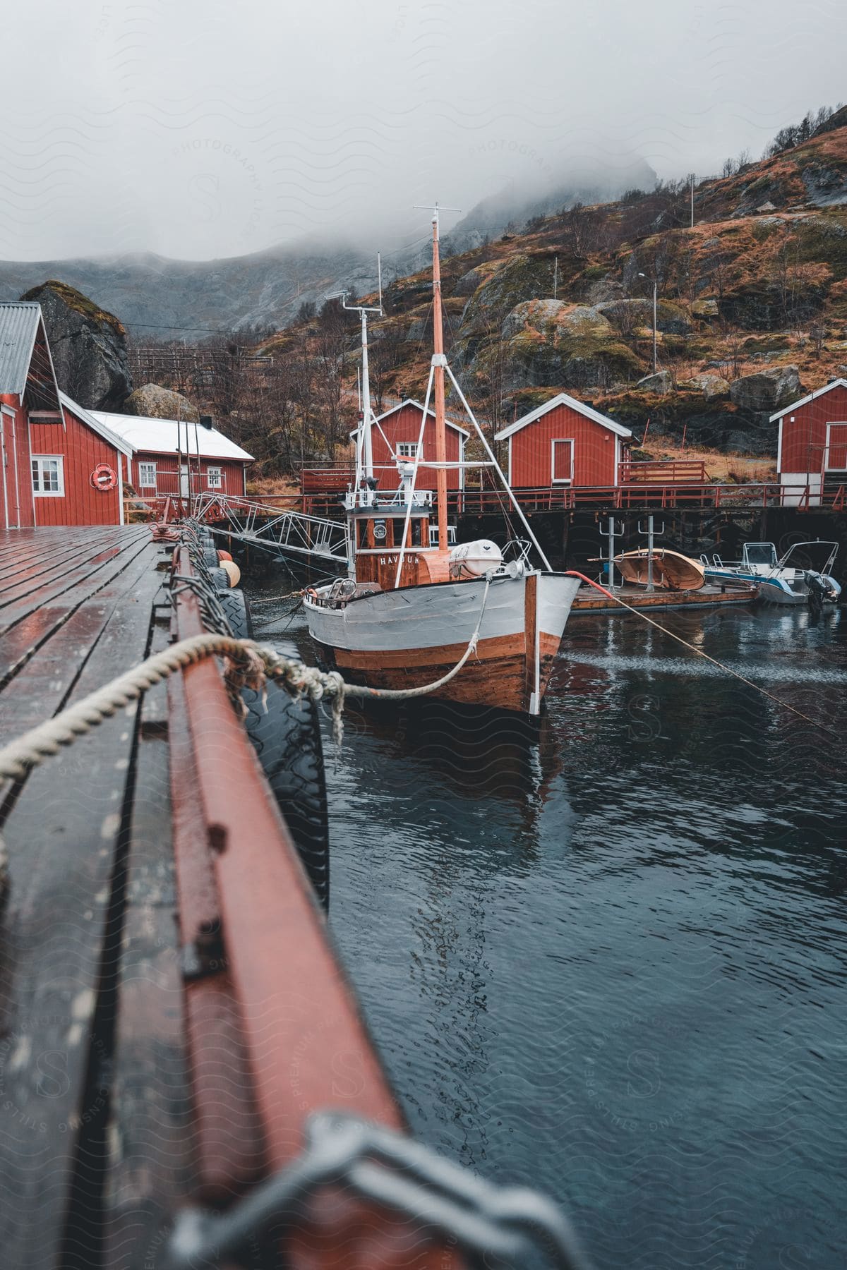 Dock on lake with rustic boat houses fishing boat and cloud cover during the day