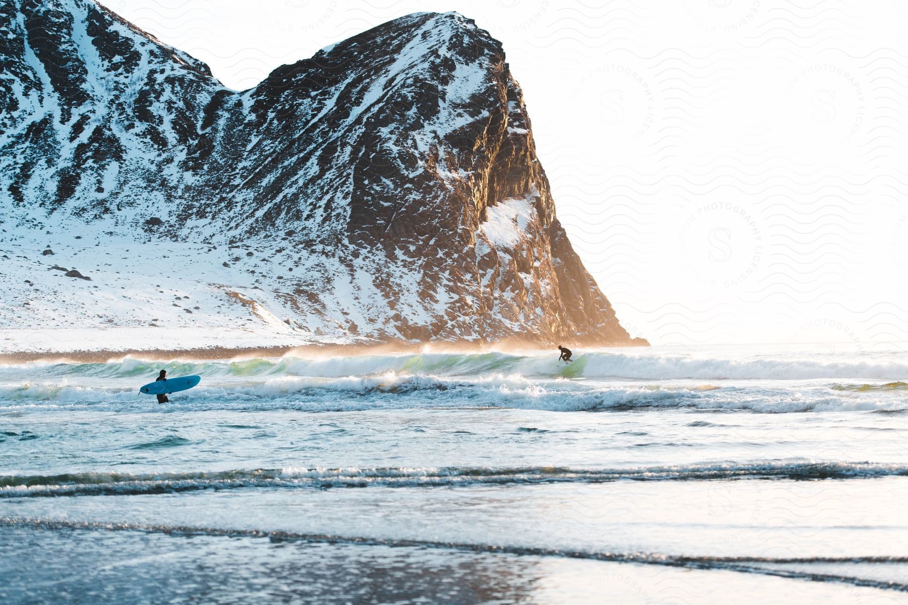 Two people enjoying a surfing adventure on a beautiful beach with mountains in the background and a serene sea