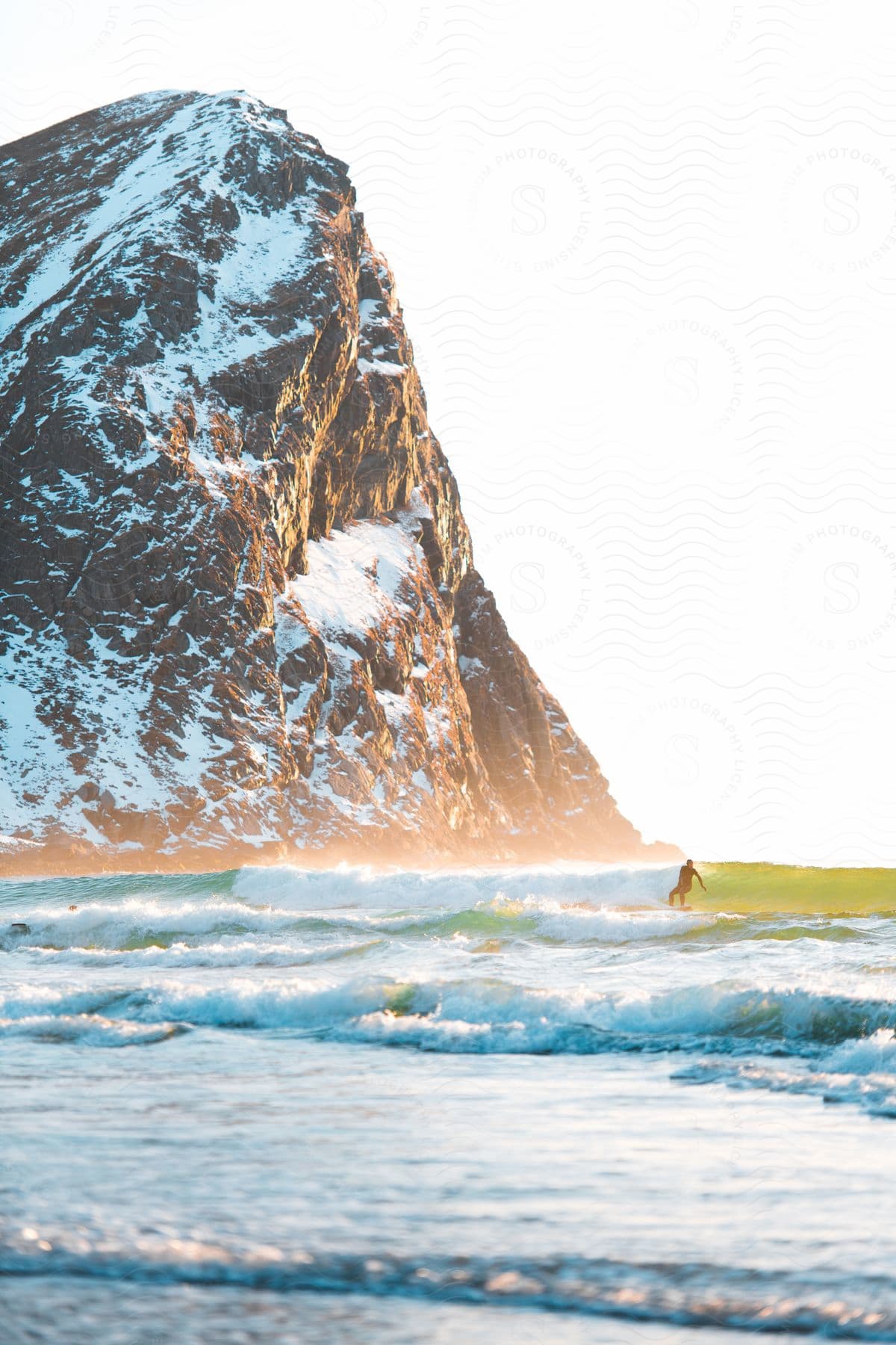 Man surfing on the sea during dusk or dawn next to a promontory