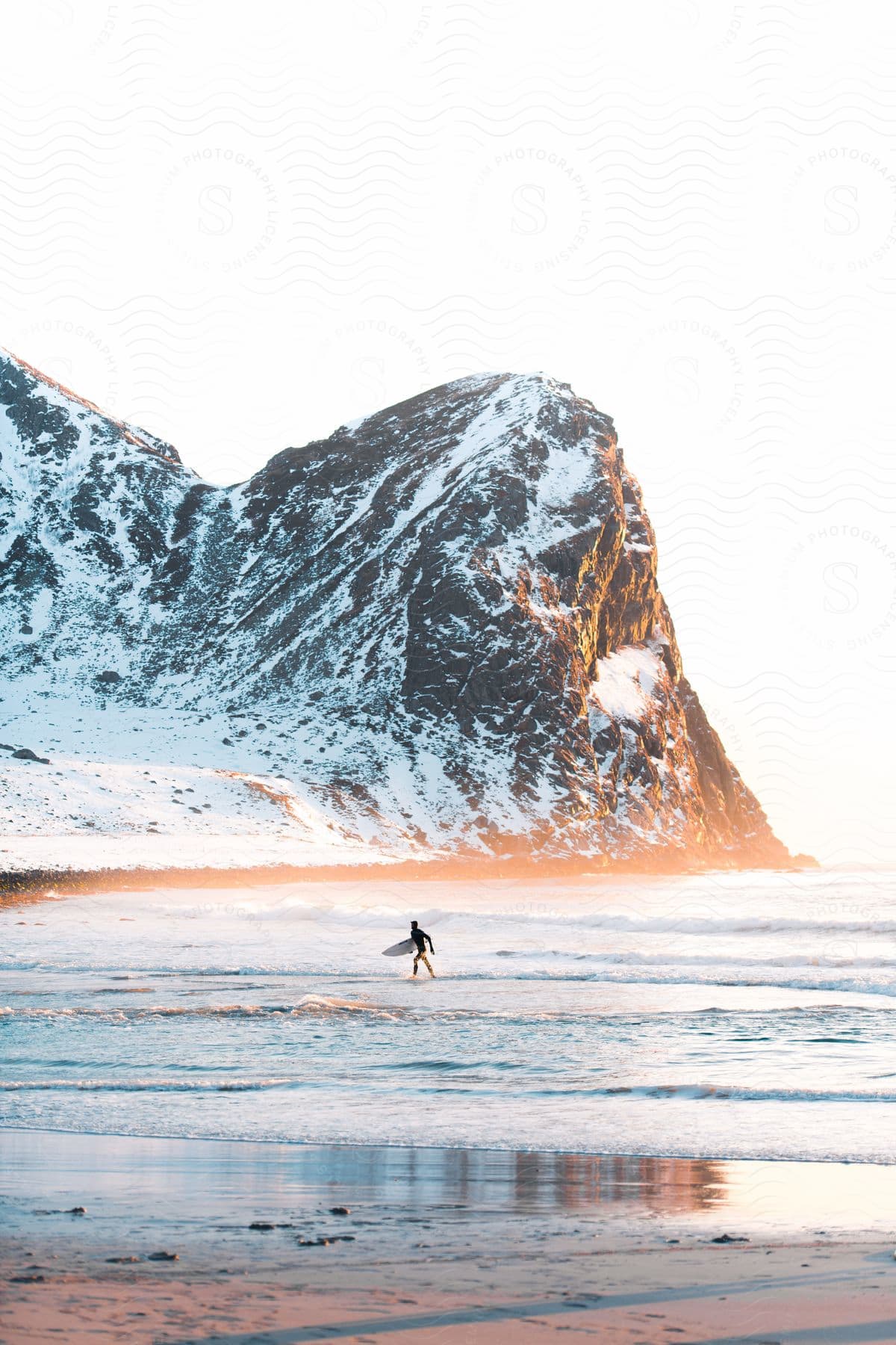 A man walking out of the ocean with a surfboard during the winter