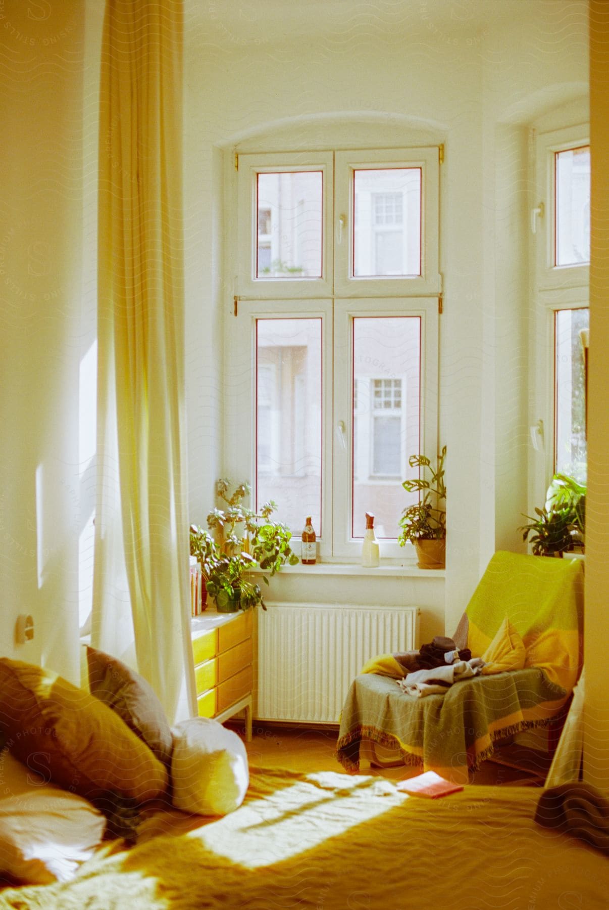 Bedroom alcove with bare windows sitting chair floor pillows room curtain wall small kneehigh dresser in a mustard yellow aesthetic on a sunny day