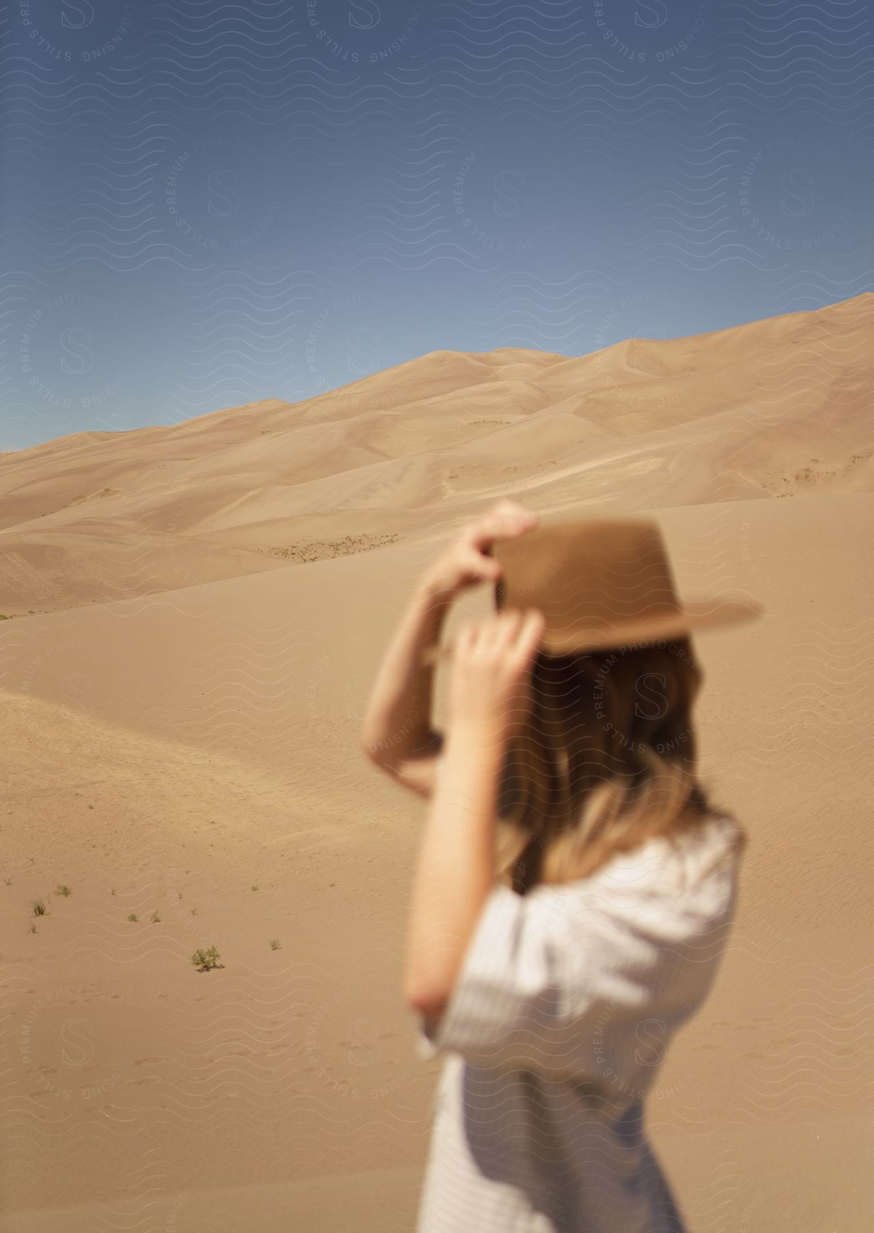 A woman holds her hat in sand dunes