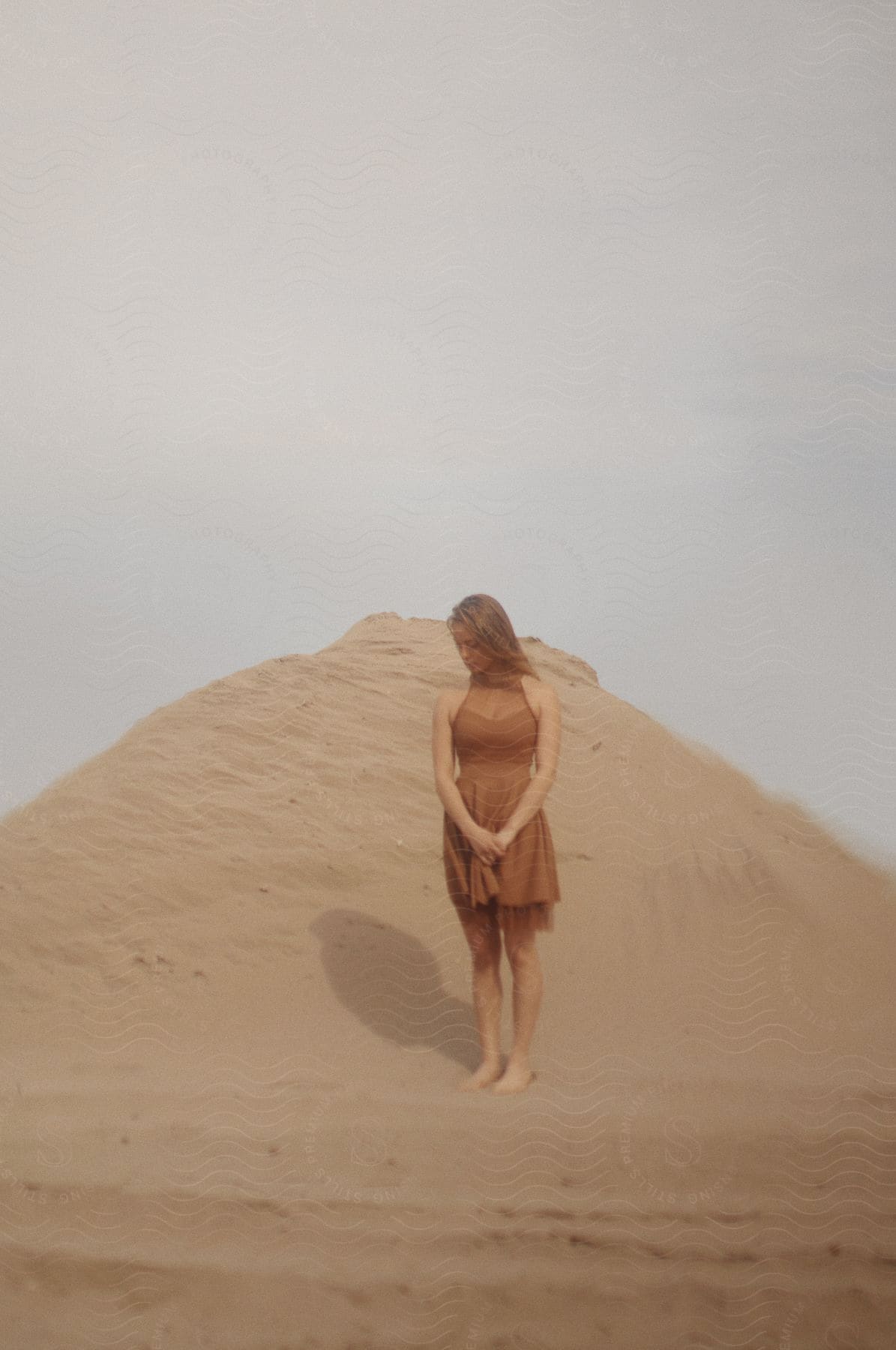 A woman in a brown dress stands in front of a sand dune