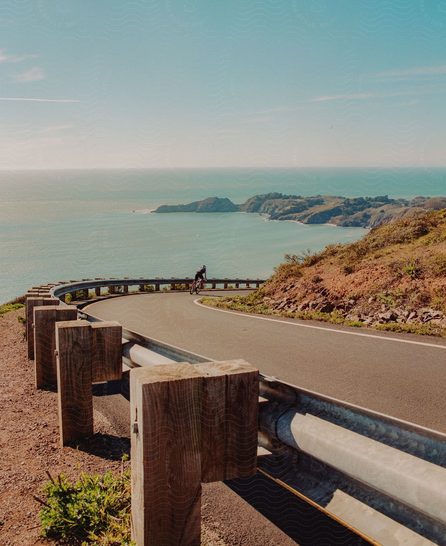 A cyclist rides their bike around a curve on a coastal road