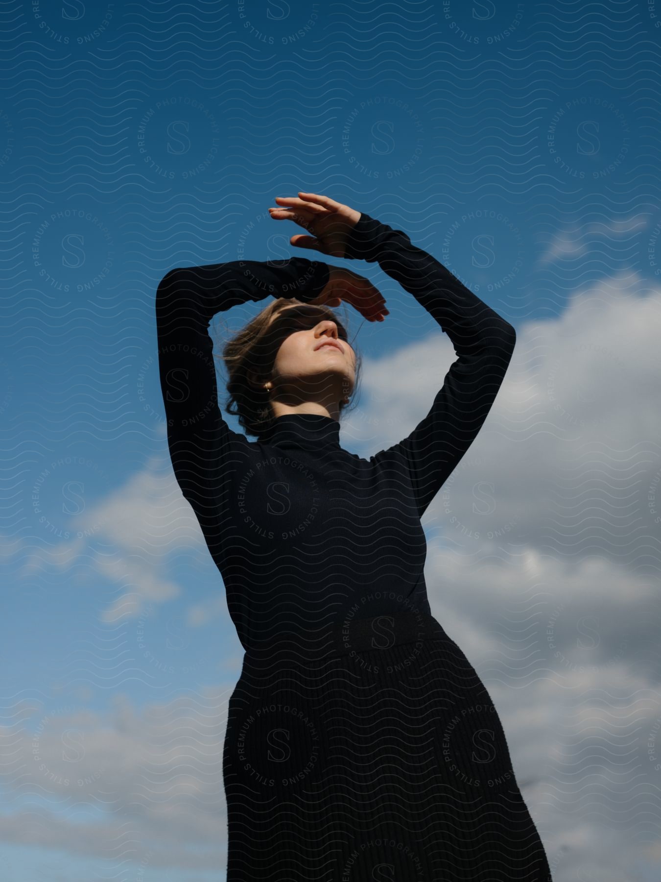 A woman in a formal dress with a smile standing outdoors with her hand raised