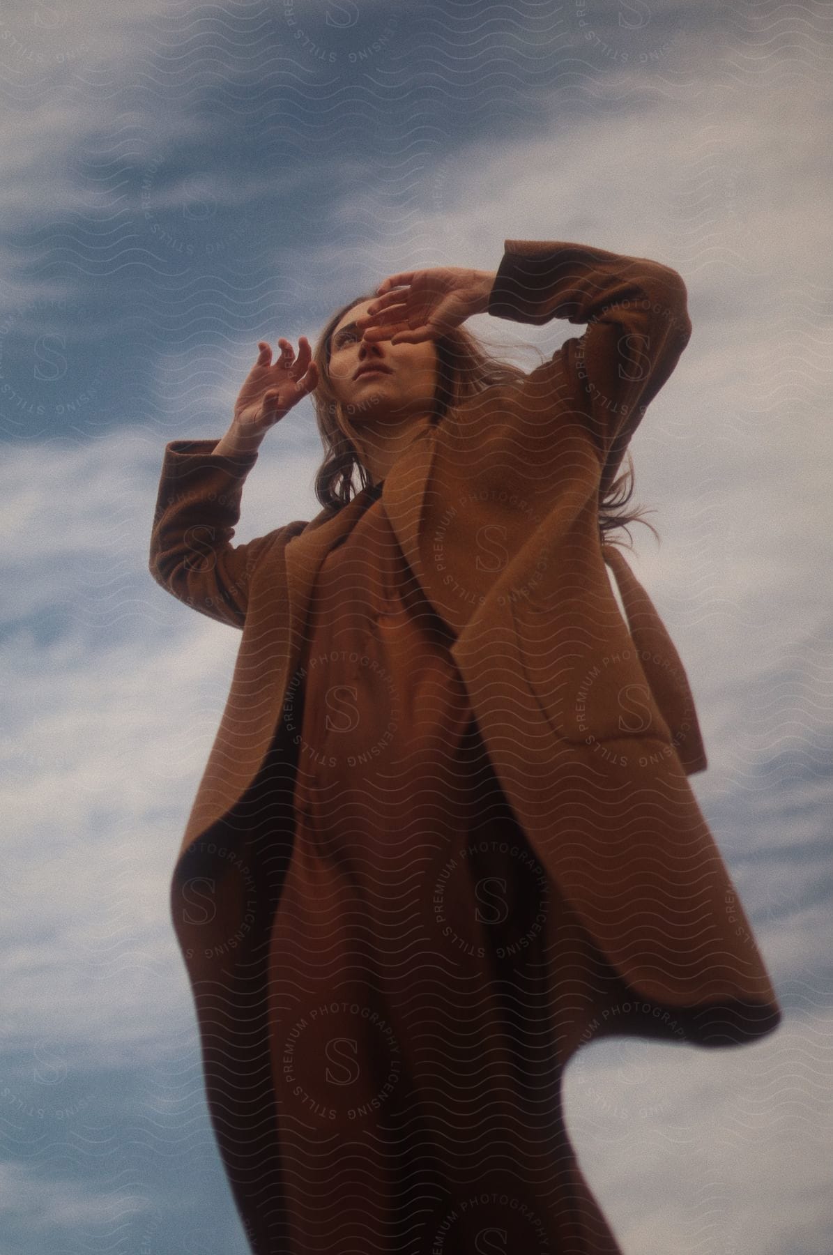 Woman wearing a coat making hand gestures under a blue sky