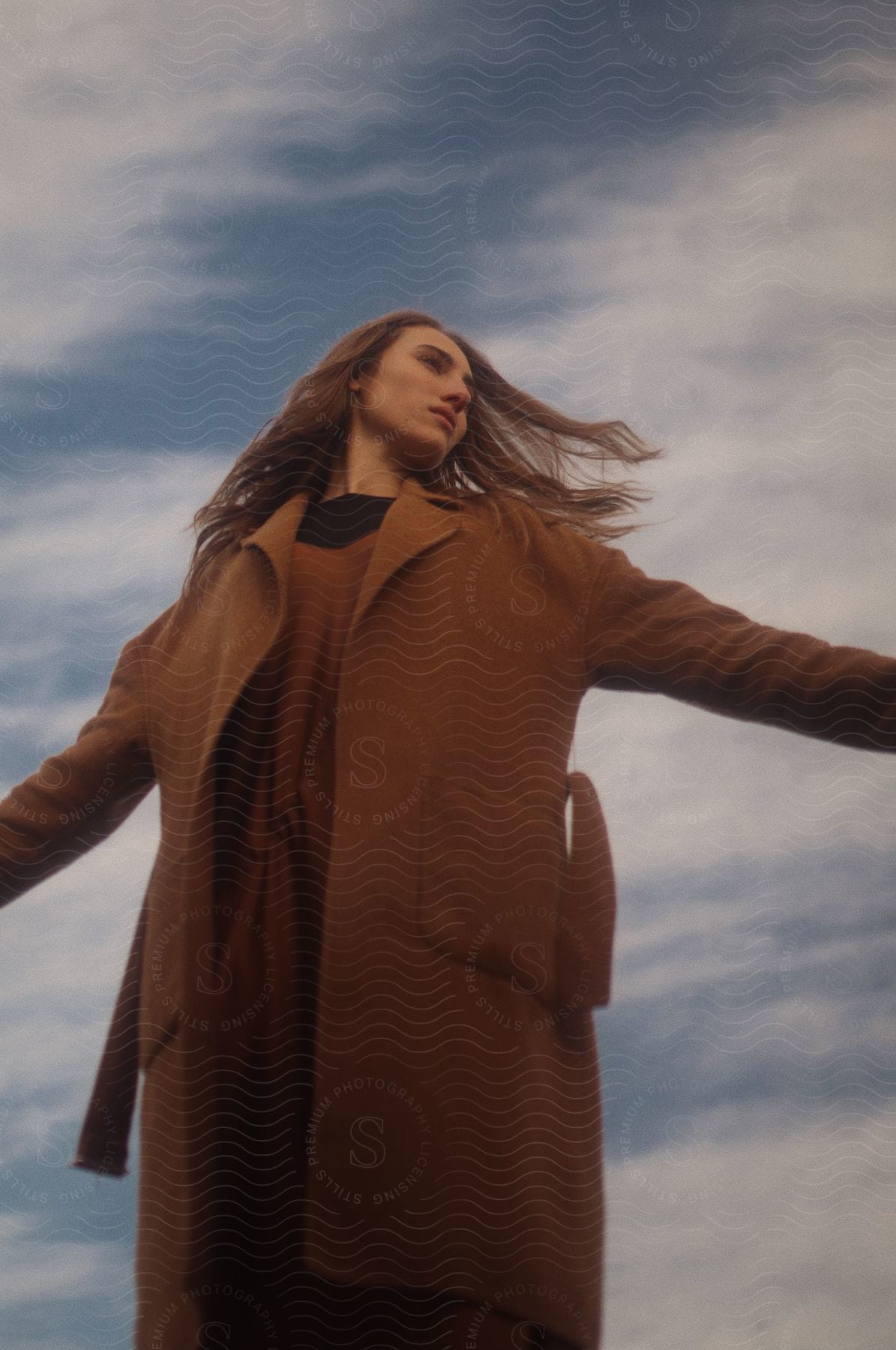 Woman in cool trench coat stretches arms wide feeling freedom and wonder in vast sky