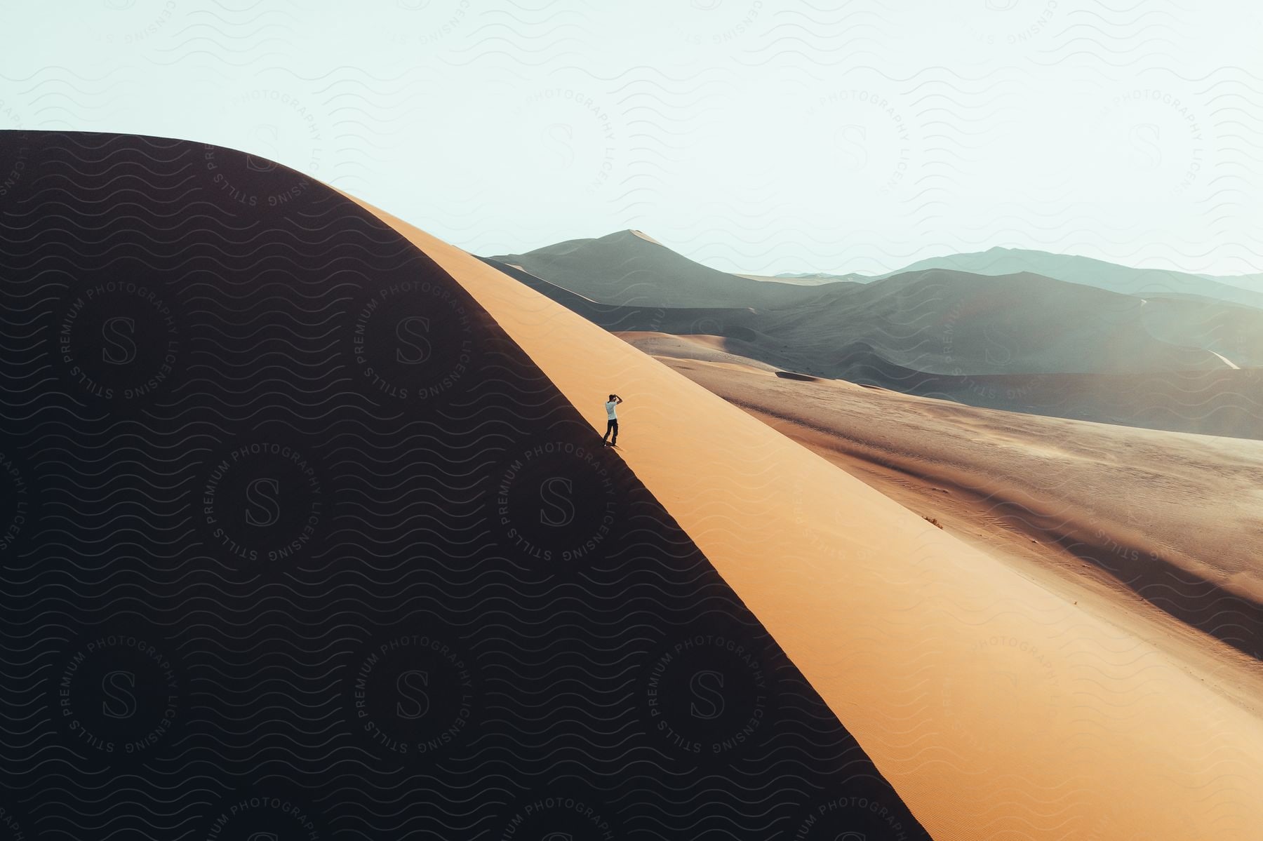 Man dressed in white looking away at the horizon in the middle of the desert next to a sand dune