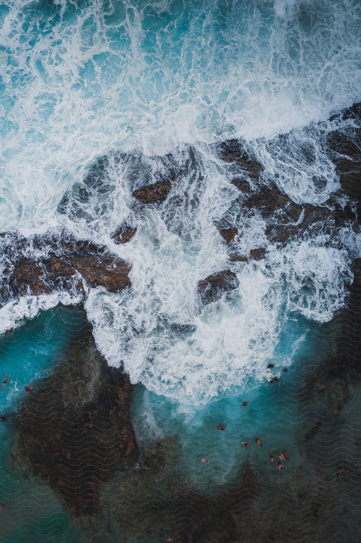 People standing on a beach next to crashing waves as seen from above