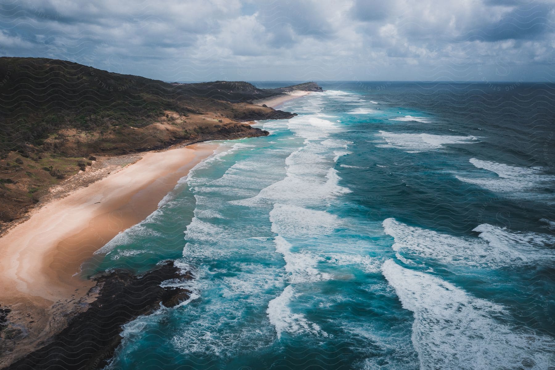 Waves roll into shore and over the beach under a cloudy sky