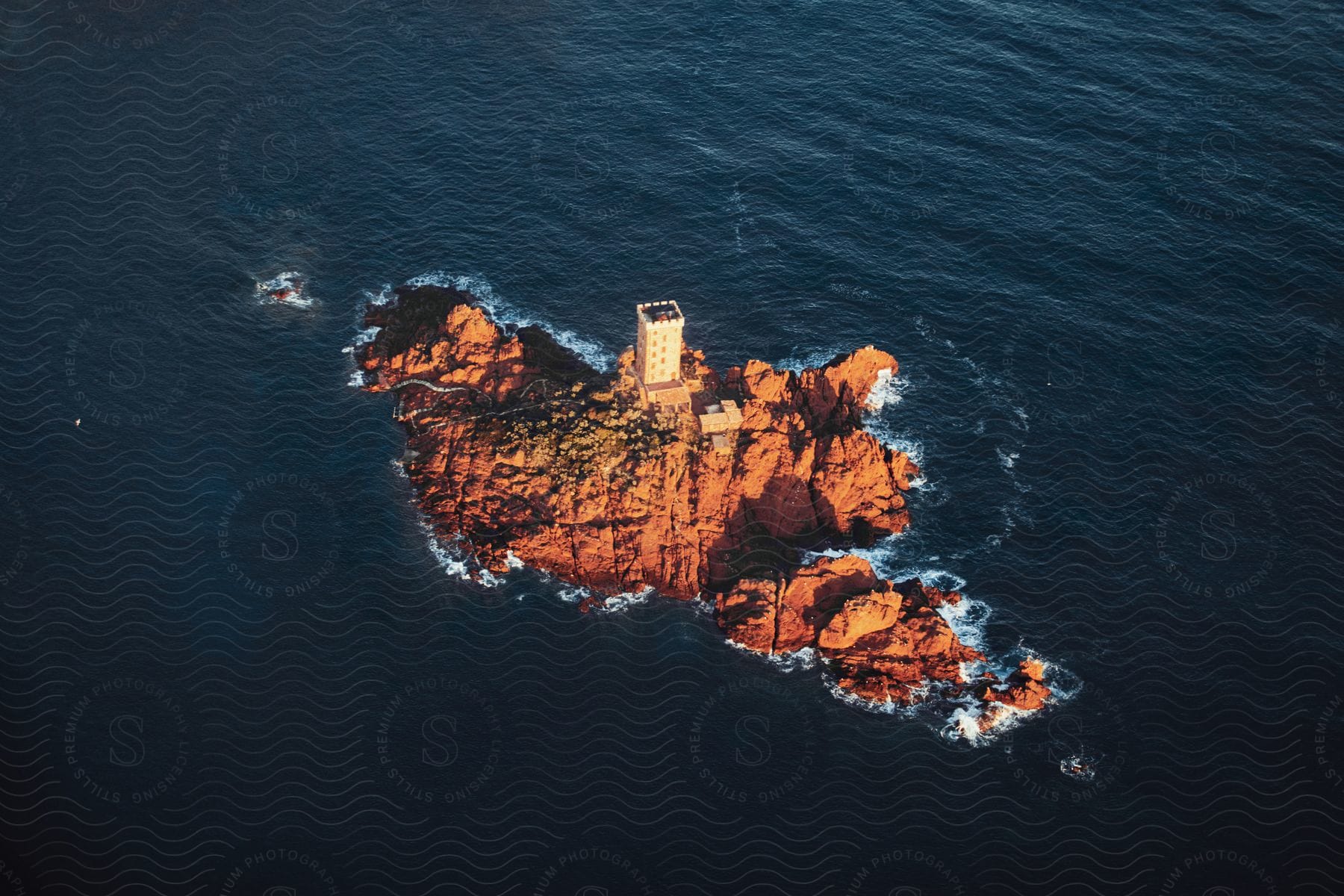 A watchtower on a small island is illuminated by the sun as waves crash onto the rocks along the coast