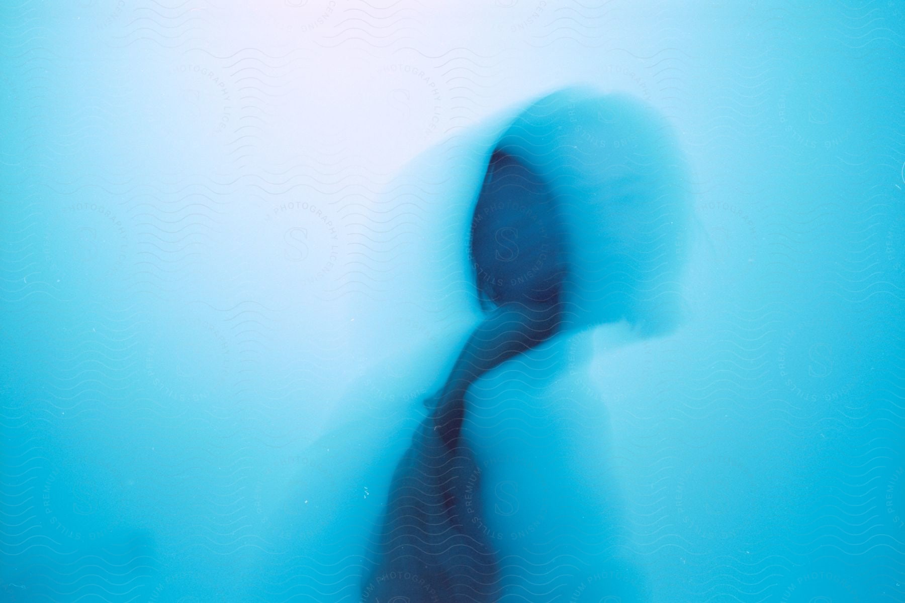 A figure stands in a softly lit blue room partially obscured by blurriness creating an ethereal ambiance