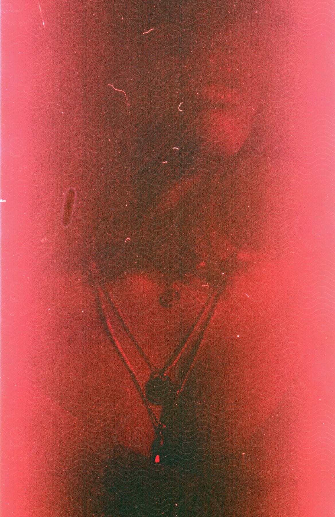 Abstract portrait of a womans face and breast covered in shadows under a red light and textured surface