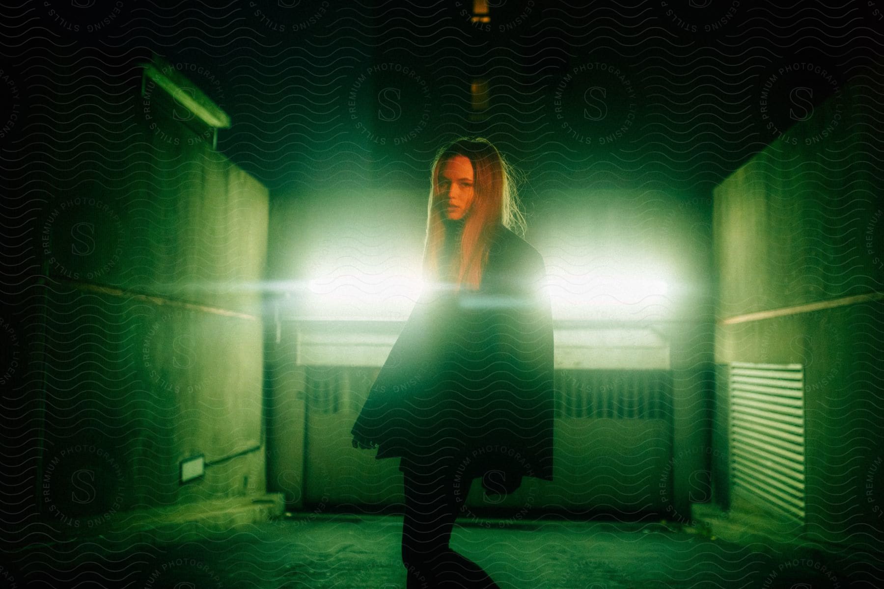 A woman wearing black stands in a room filled with green light as glowing beams shoot through her