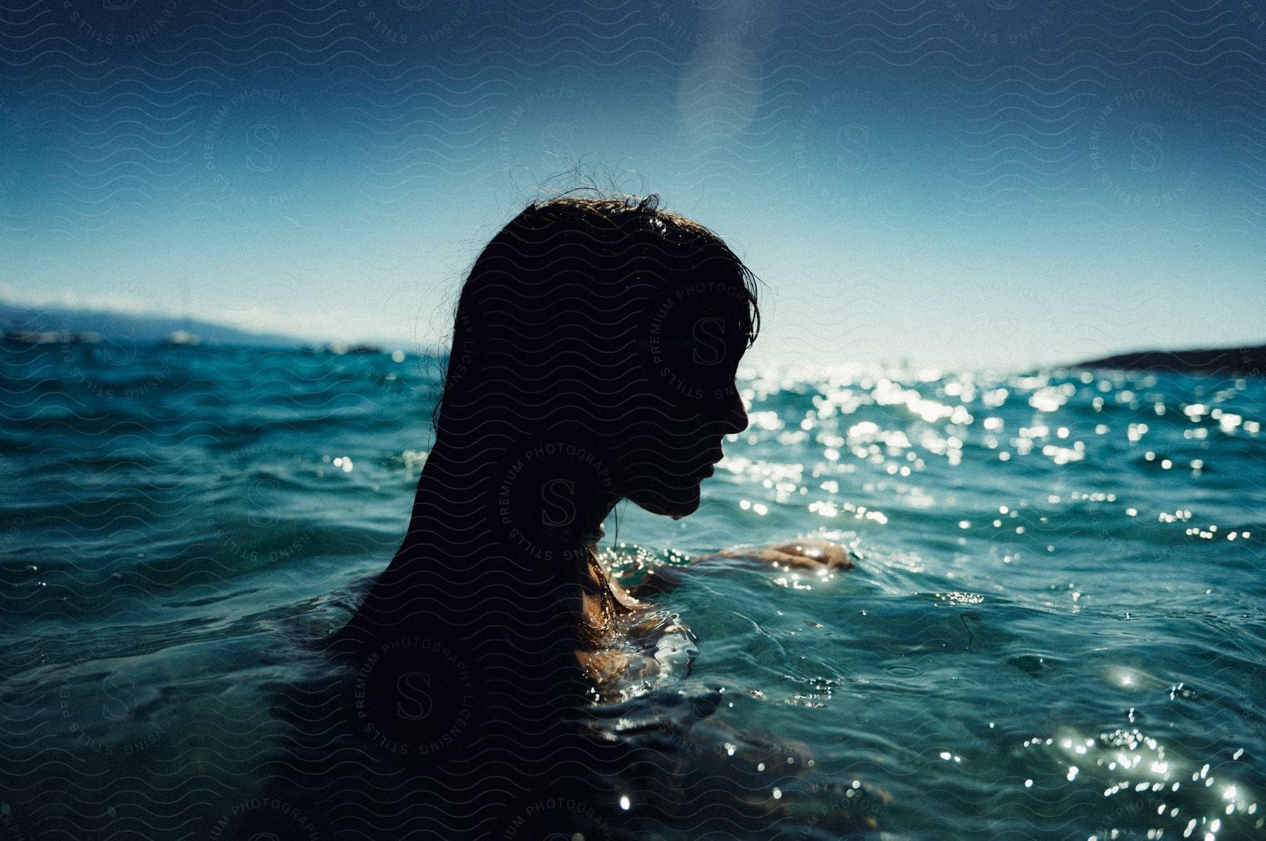 A womans silhouette above water with sun reflecting off the surface