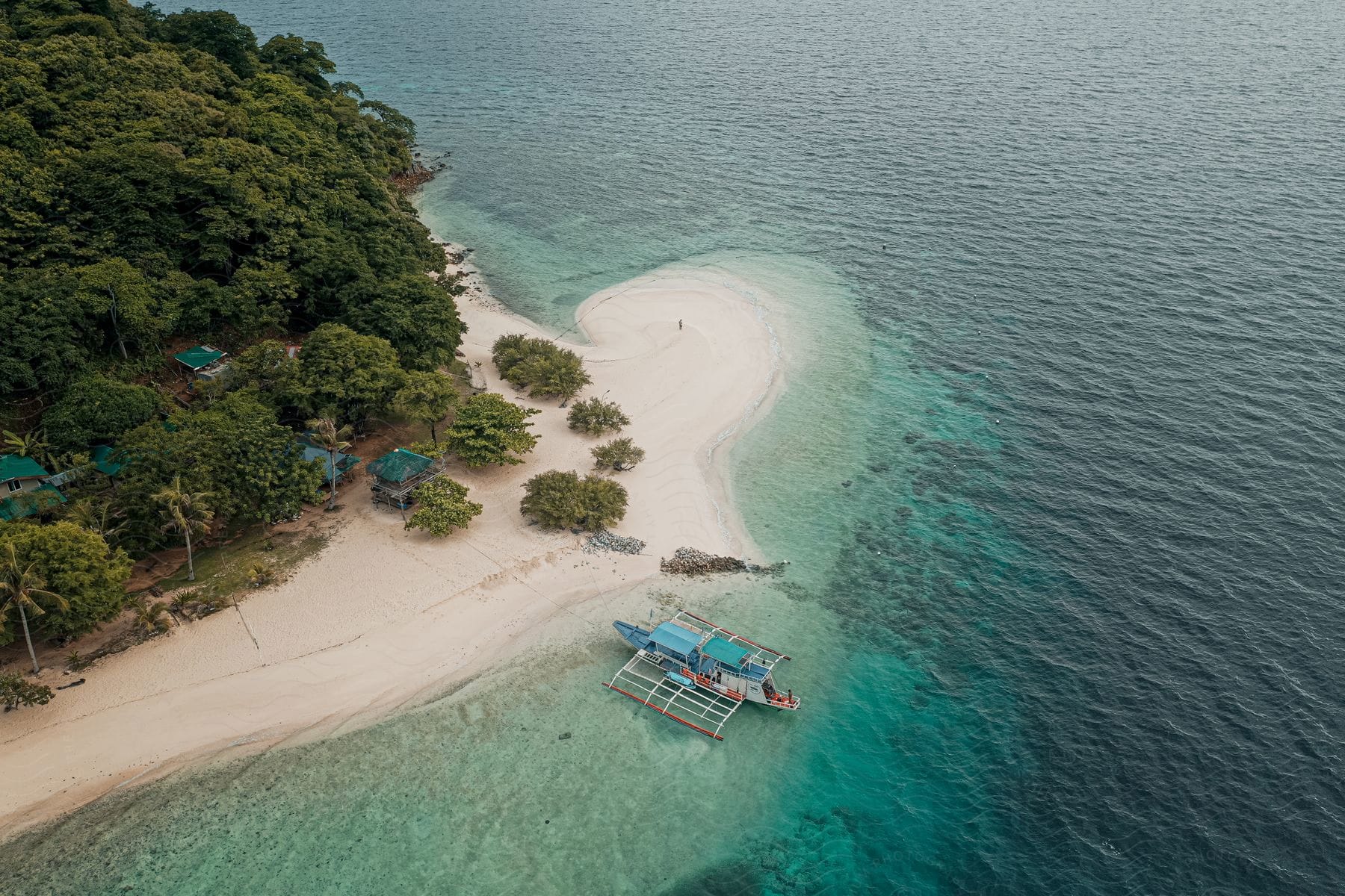 Island surrounded by water with small huts trees and a boat on the shore