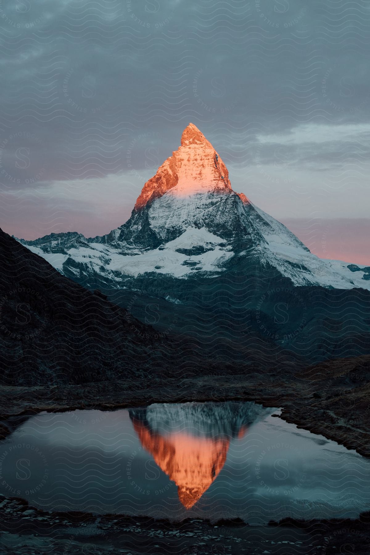 A sunlit mountain peak with a reflective lake below in the european alps