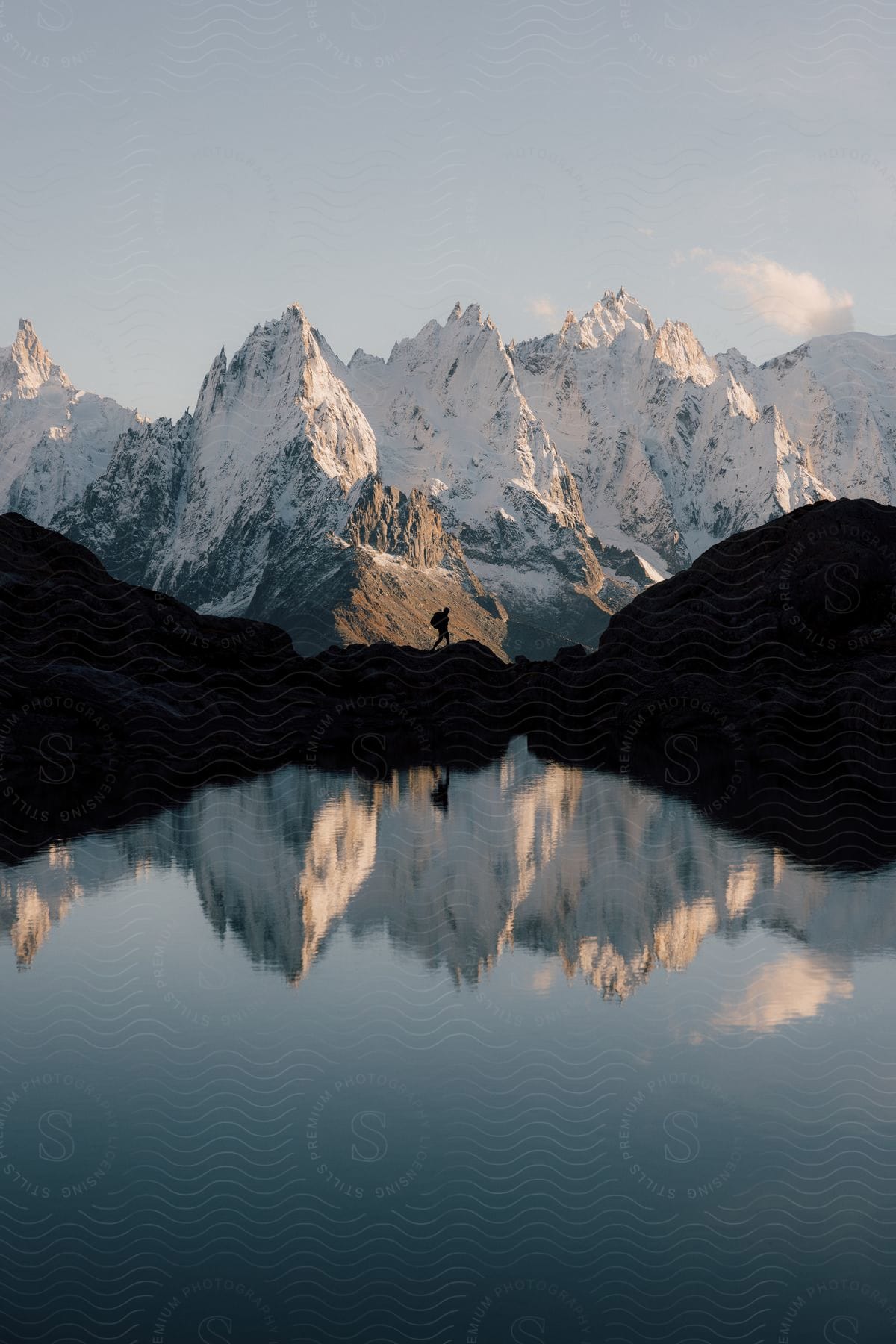 A person walking on a rocky path with a lake and icy mountains in the background