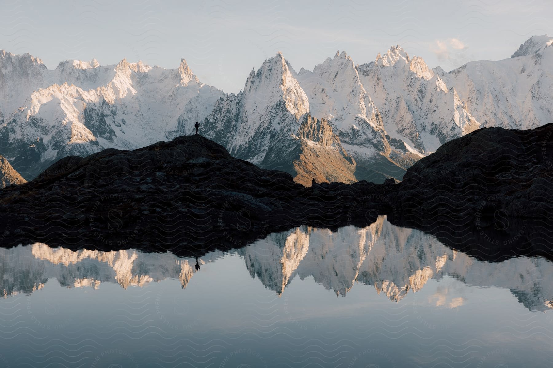 A lone hiker stands near a lake surrounded by snowcovered mountains in the european alps