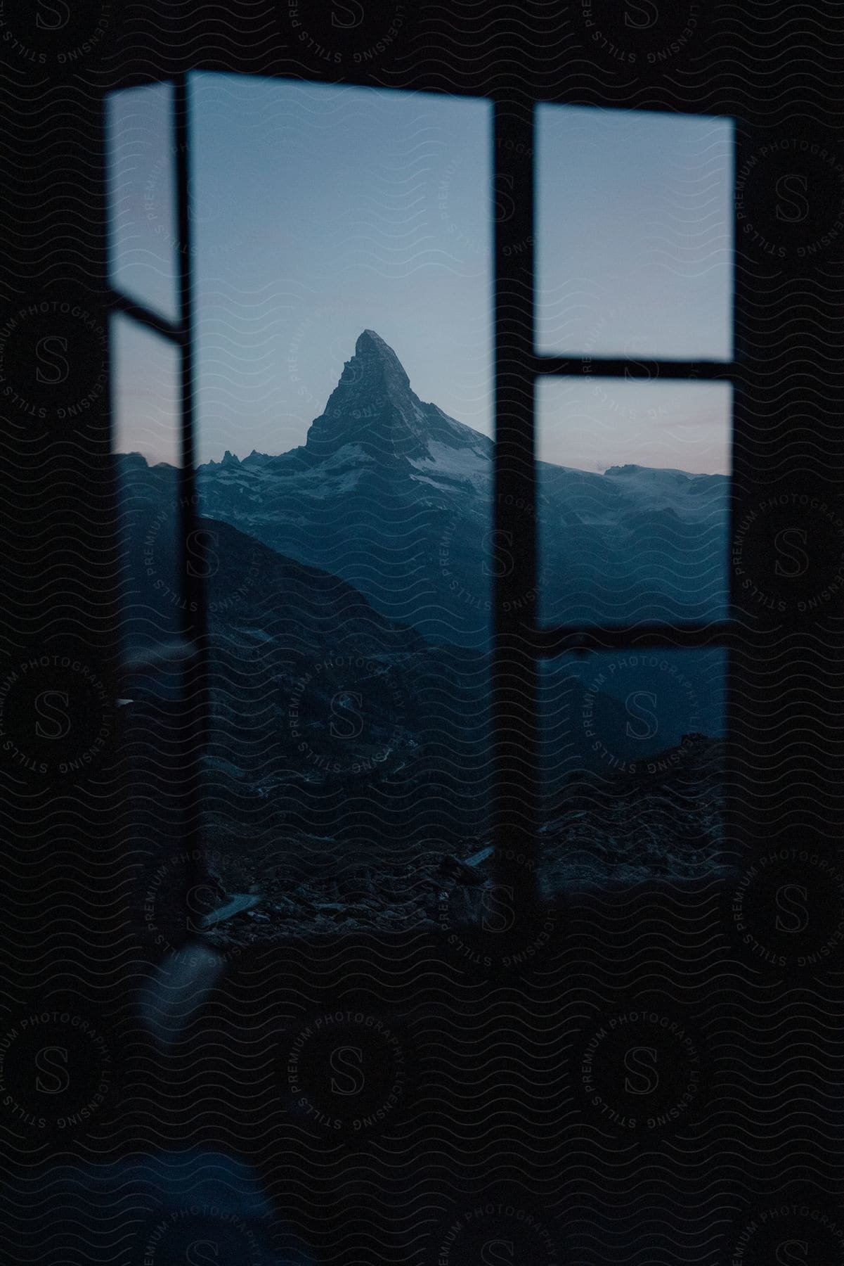 Snowy mountains against a pale blue sky seen through an interior window at dusk