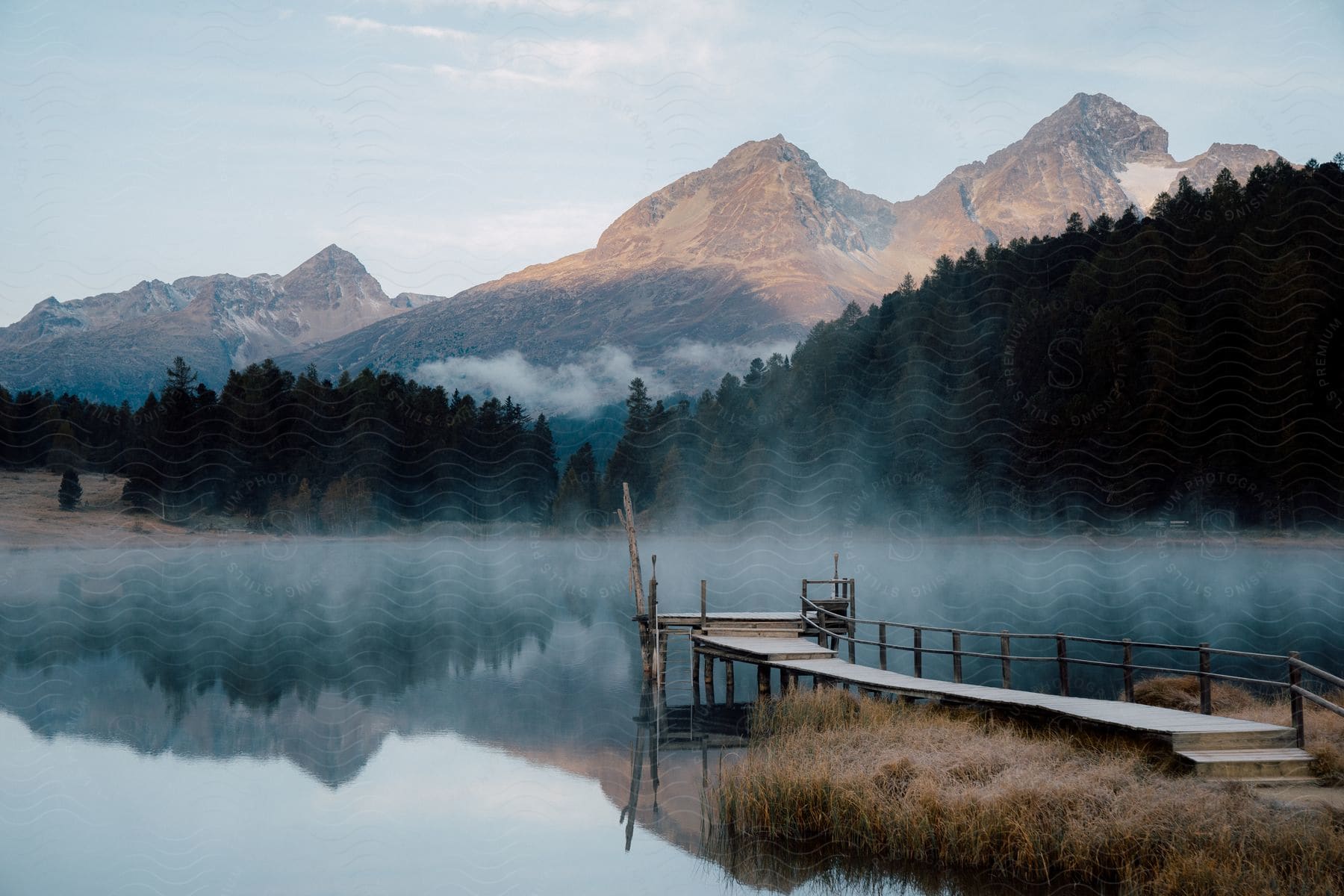 A wooden pier at a lake surrounded by forests and mountains