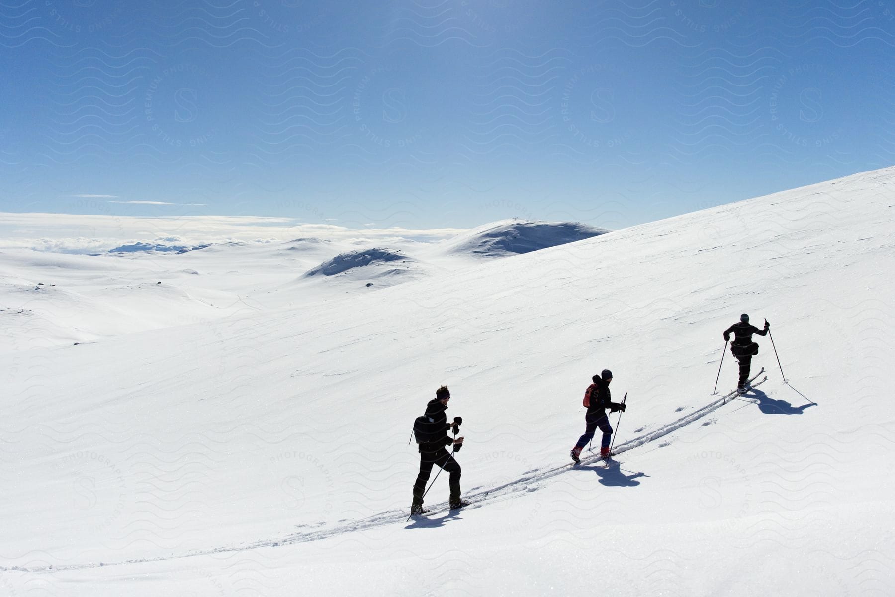 Three people are skiing up a mountain on a sunny day with a blue sky