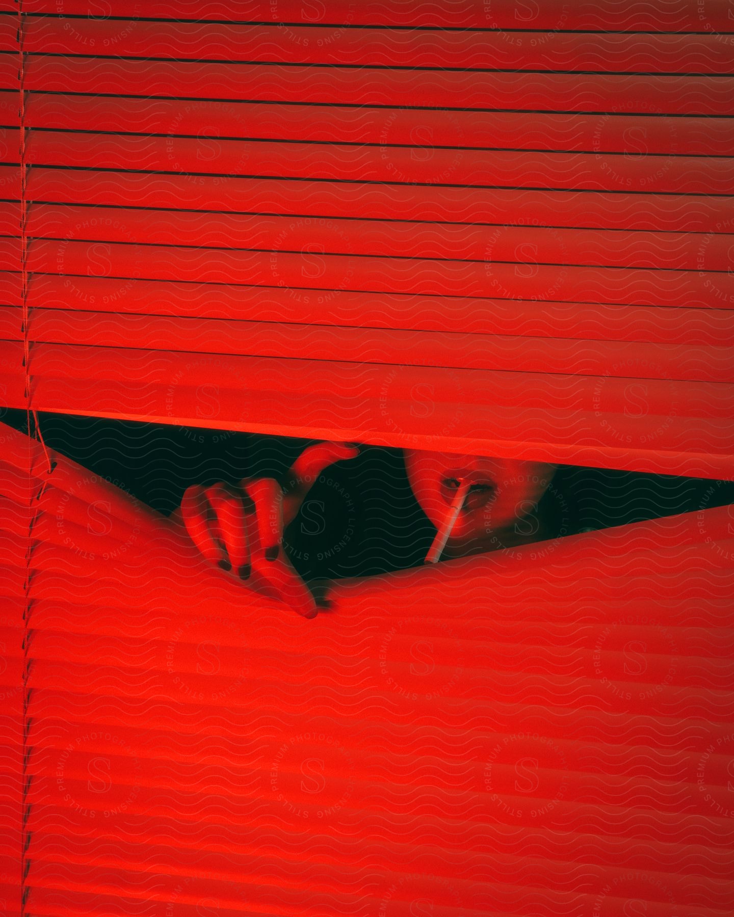 A woman with a cigarette in her mouth reaches through blinds in red light