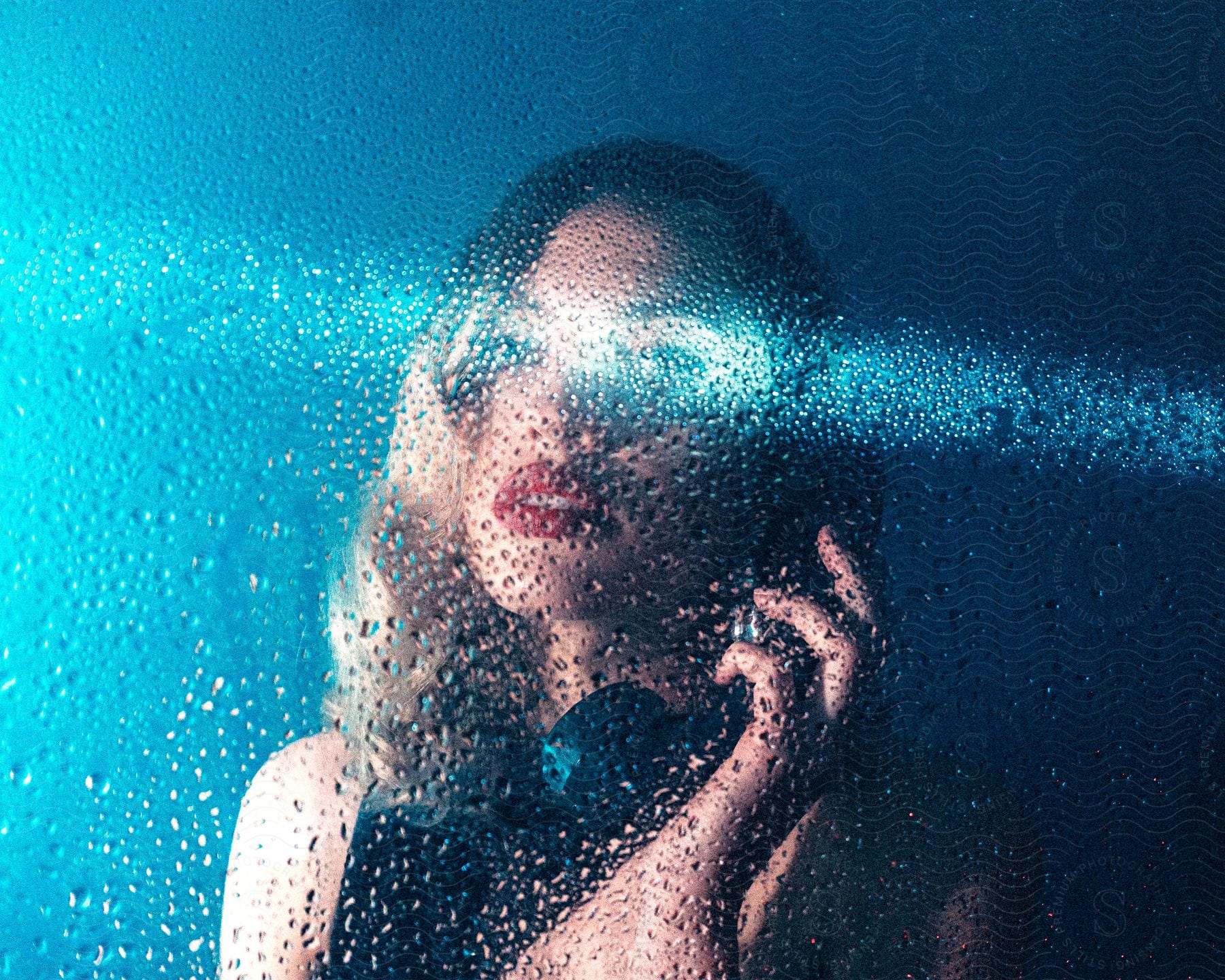 A woman talks on the phone behind a wet glass surface