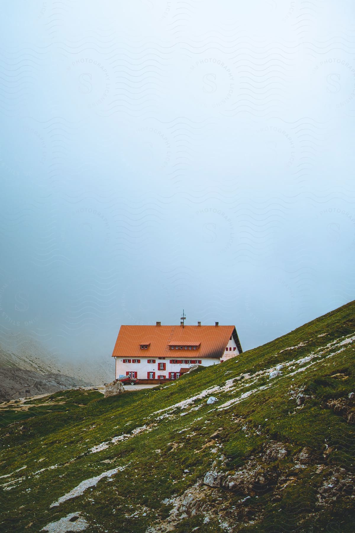 A house rests on a grassy hillside lightly covered in snow on a misty day in the dolomites