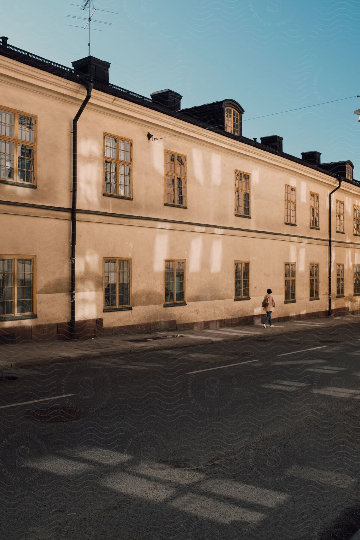 A woman walking on a sidewalk near a twostory building with many windows in an urban area