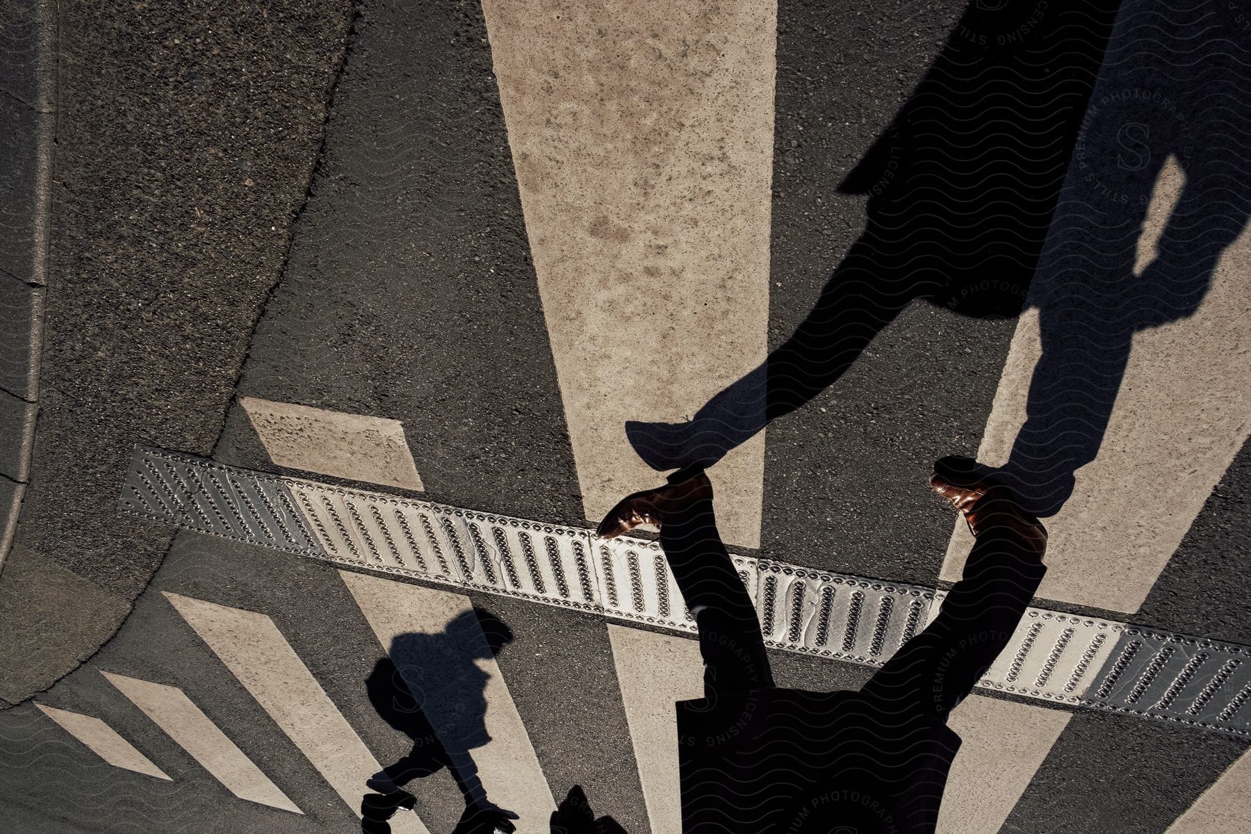 A zebra crossing sign with two mens feet walking casting shadows on the ground