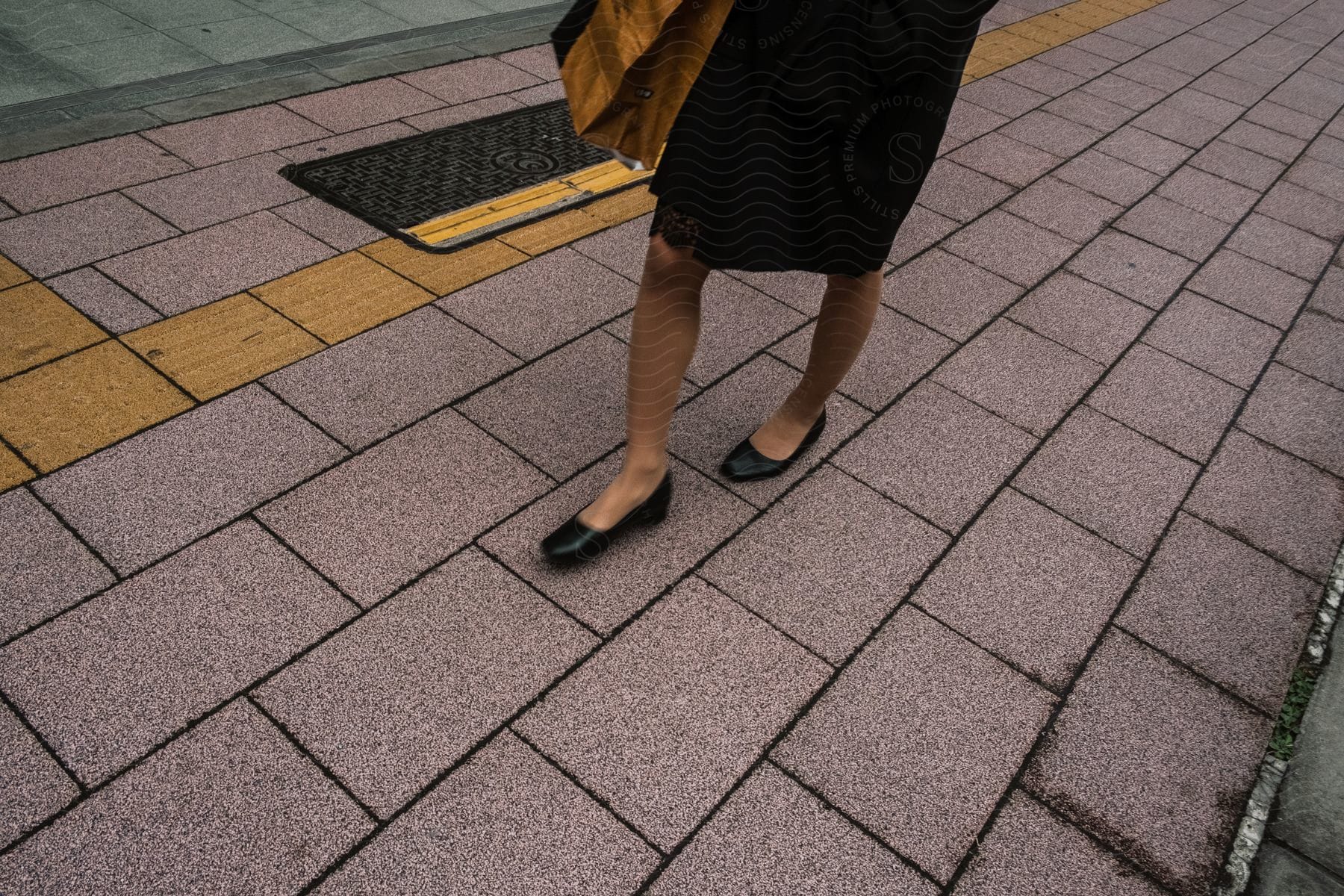 A woman in black flat shoes walks on the concrete city sidewalk