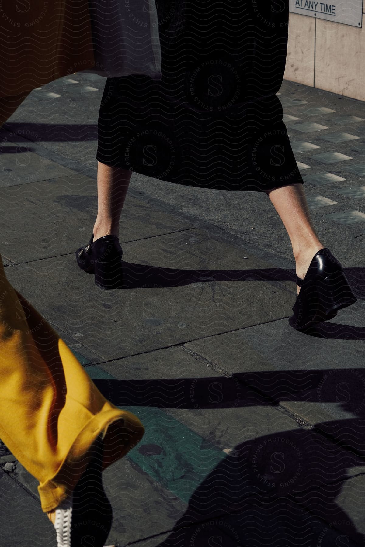 A person walking on a grey road wearing black high heels