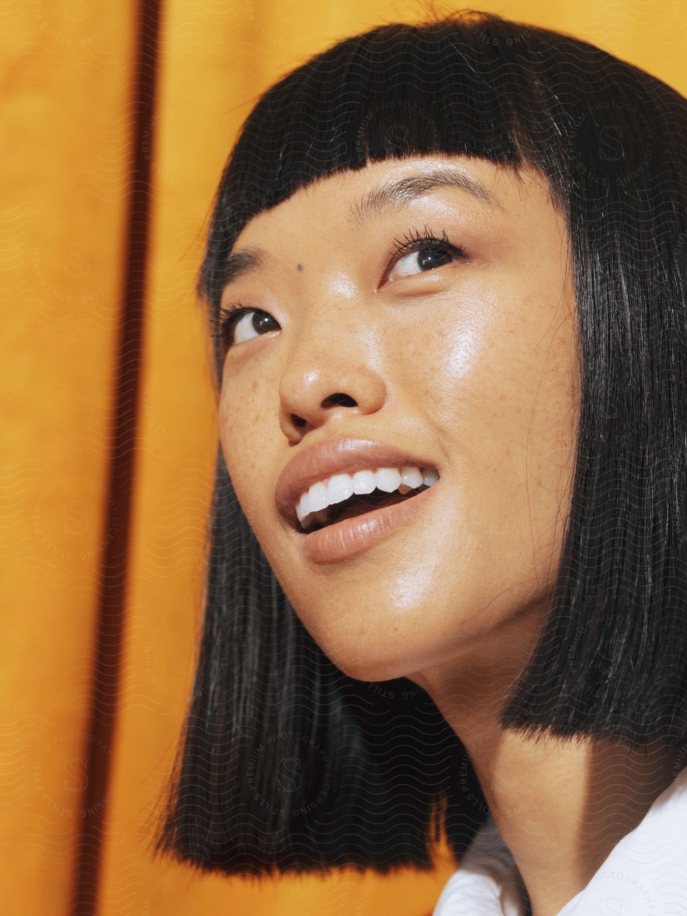 Woman with white teeth straight hair and white shirt looking up and smiling brightly