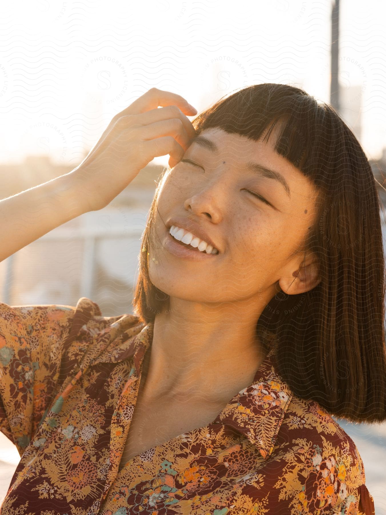 Woman with black hair smiles with her eyes closed as she touches her fingers to her head