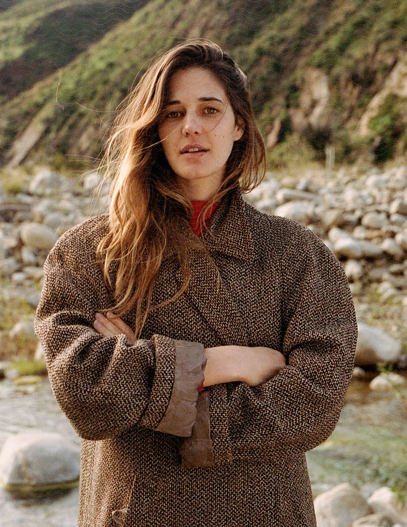 A woman in a sweater jacket and coat stands in a field with a happy expression