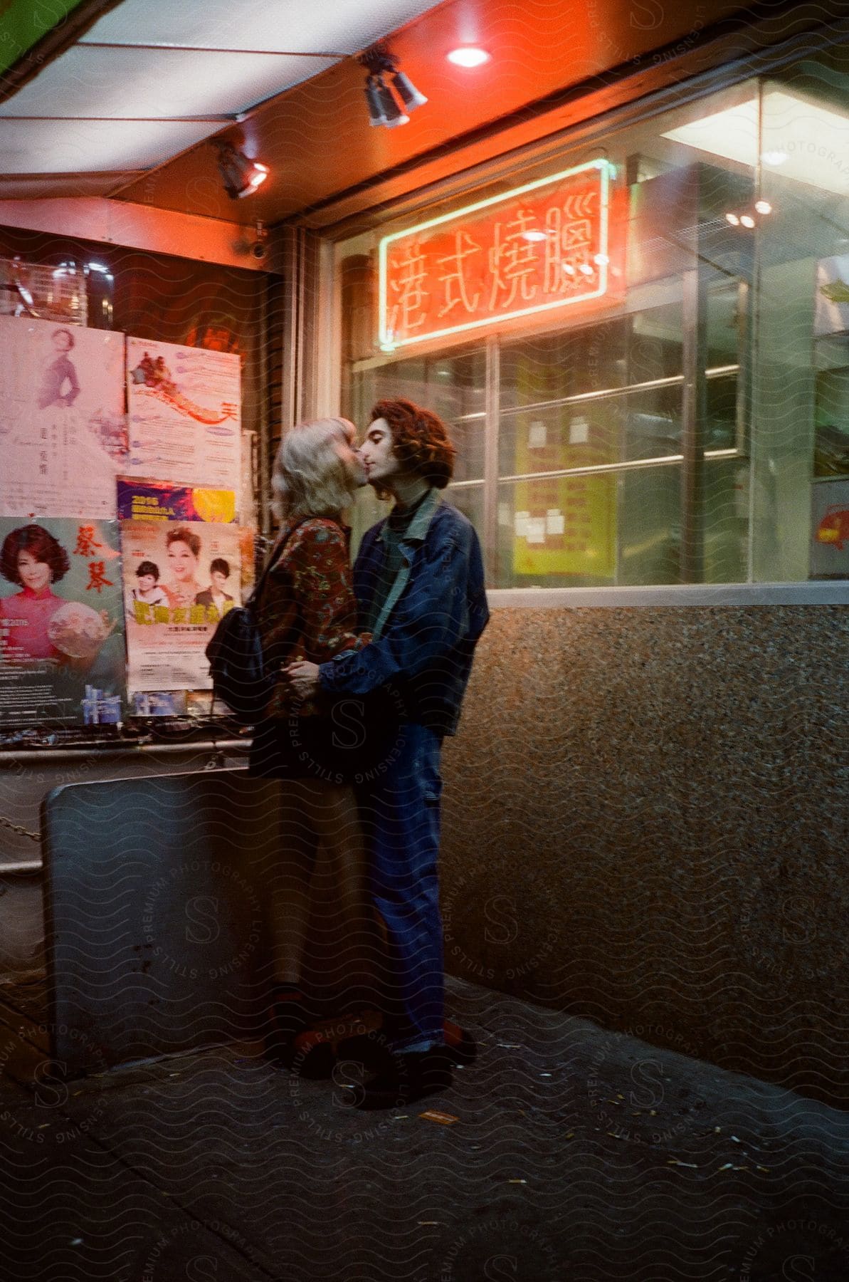 Romantic couple kissing in front of a store with a red neon sign at night in brooklyn