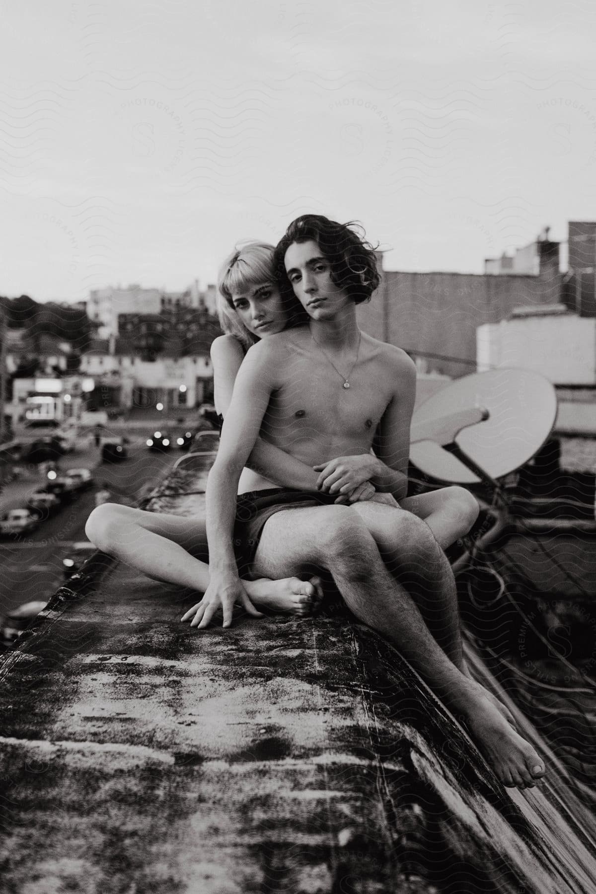 A man and woman sit on a rooftop posing for the camera with a city street in the background