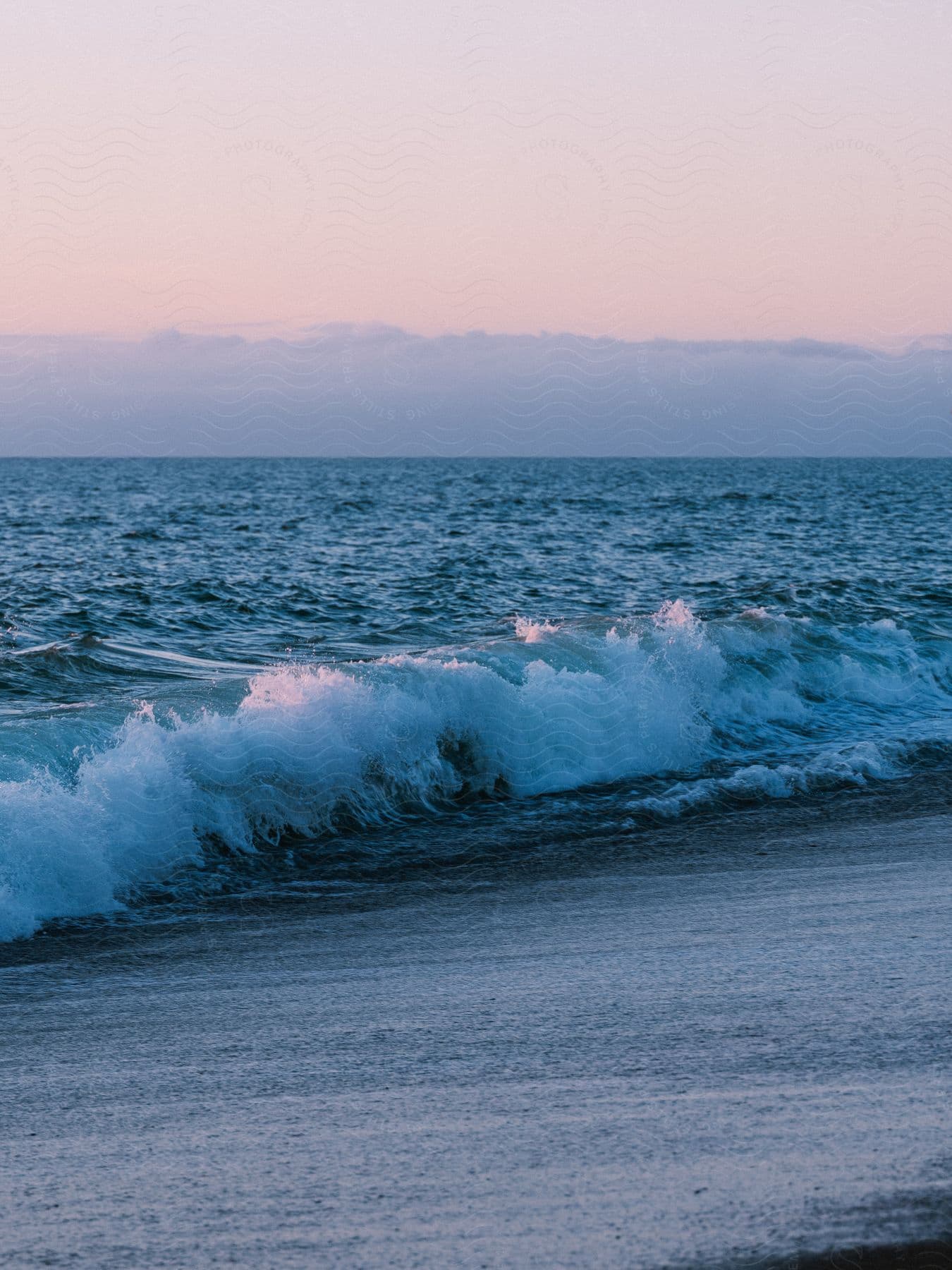 A wave crashes on the sandy beach shore