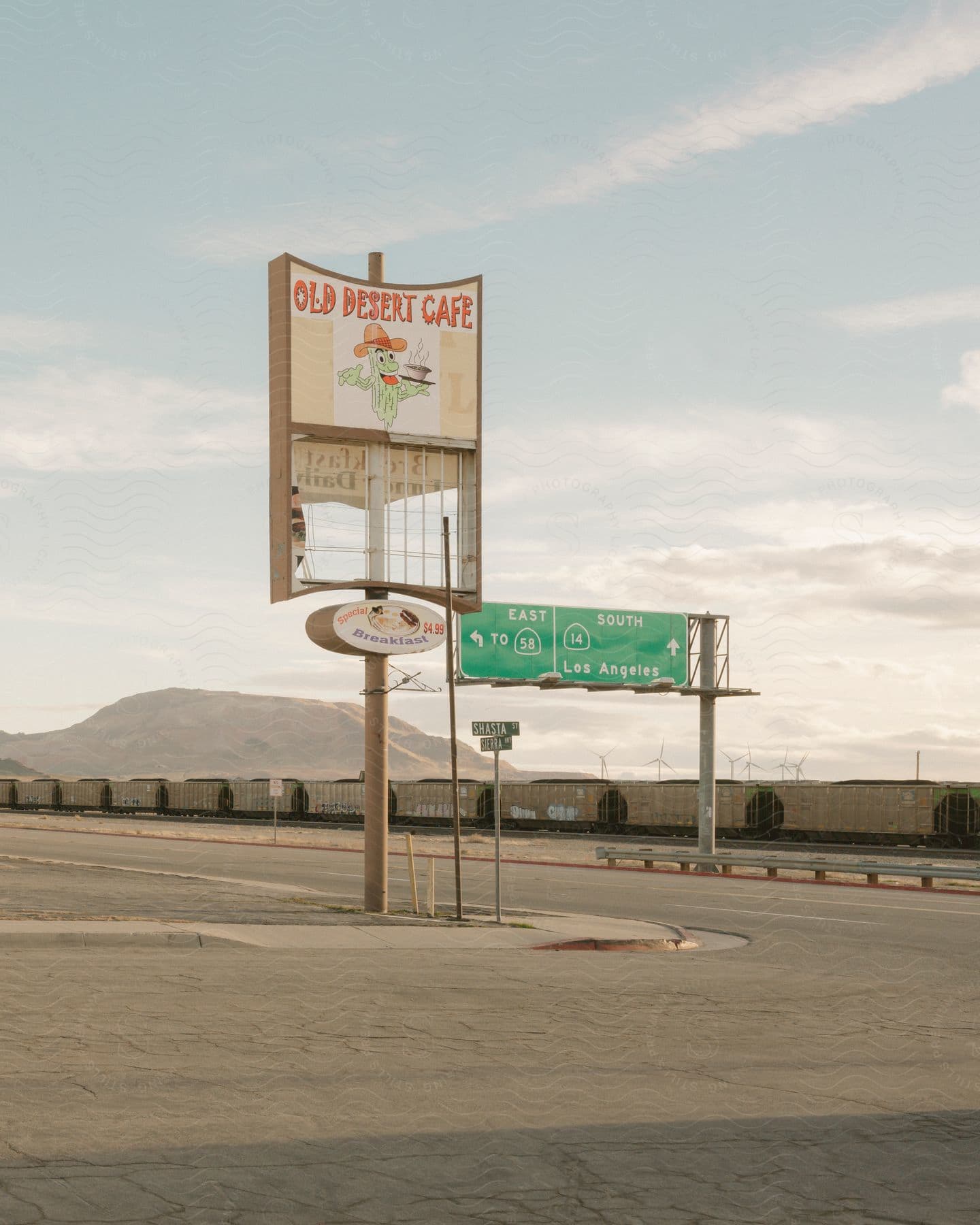 A cafe sign stands next to a highway exit sign with a freight train visible across the highway