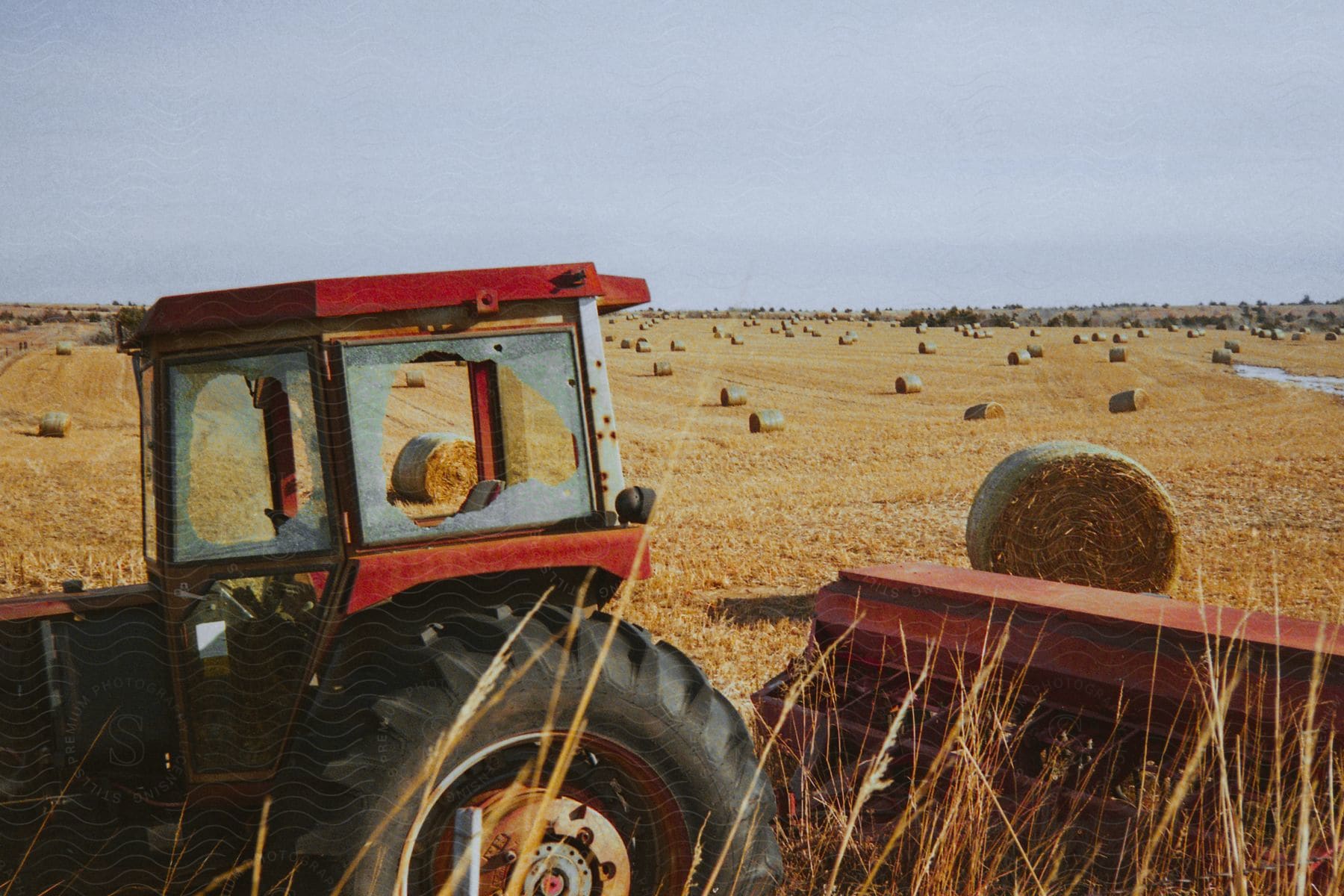 A brokenwindowed tractor with a planter attached is parked in a hay field in kansas