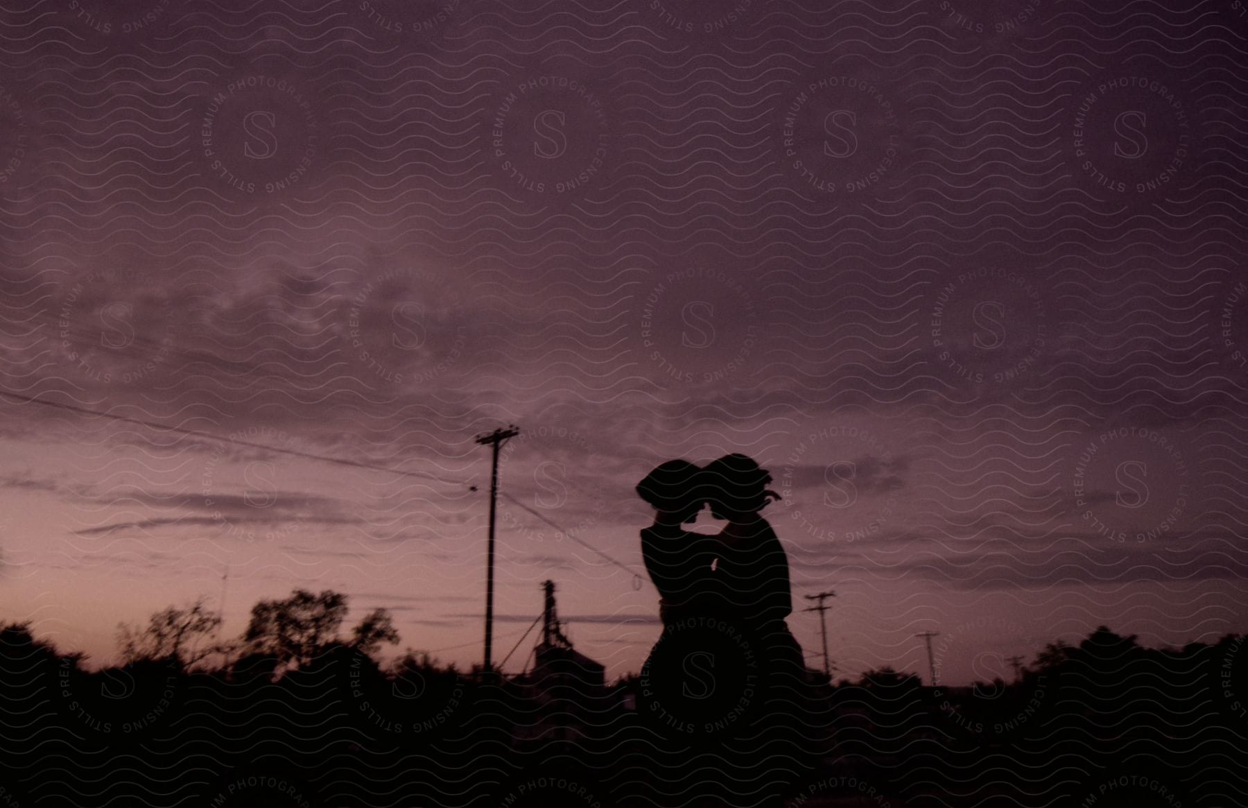 A man and woman embrace in front of a factory and power lines at dusk