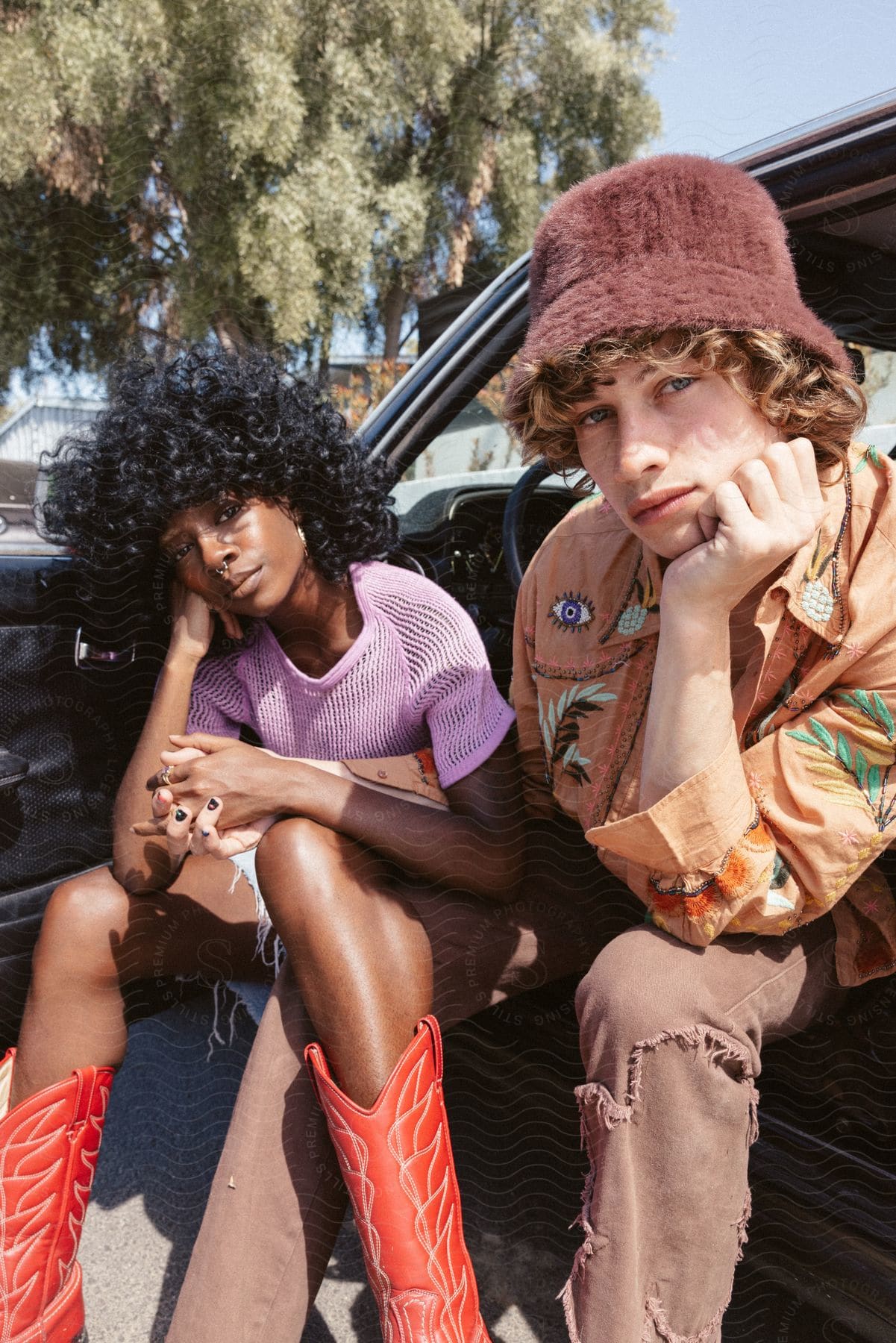 A teenage boy and girl sit in an open car holding hands