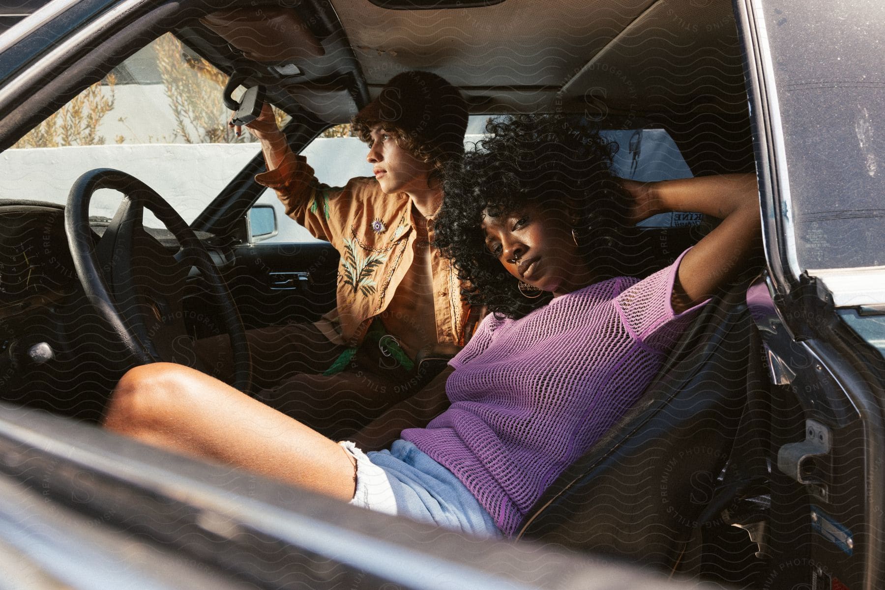 Woman with curly hair and purple shirt and man in orange jacket sit in car